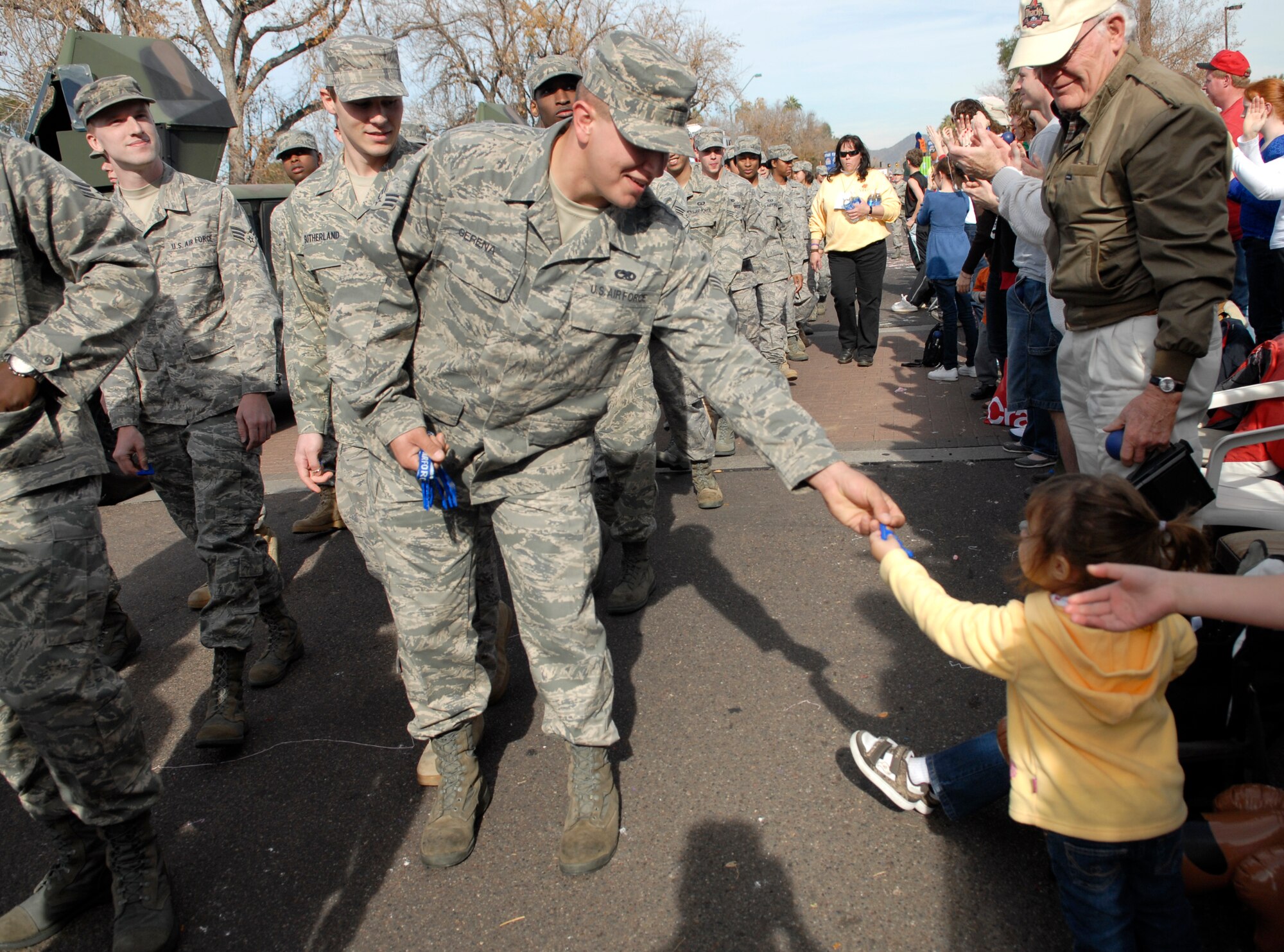 Senior Airman Josh Gerena of the 56th Aircraft Maintenance Squadron hands out a keychain to a child as a group of Airmen walks through downtown Phoenix during the 38th Annual Fiesta Bowl Parade Jan. 3. More than 100 Airmen participated in the event which is part of Phoenix's Fiesta Bowl event schedule including the Insight Bowl game in Tempe, for which Luke F-16s performed a fly-over and the Fiesta Bowl game itself in which Luke Airmen will be honored. (U.S. Air Force photo/Master Sgt. William Gomez)
