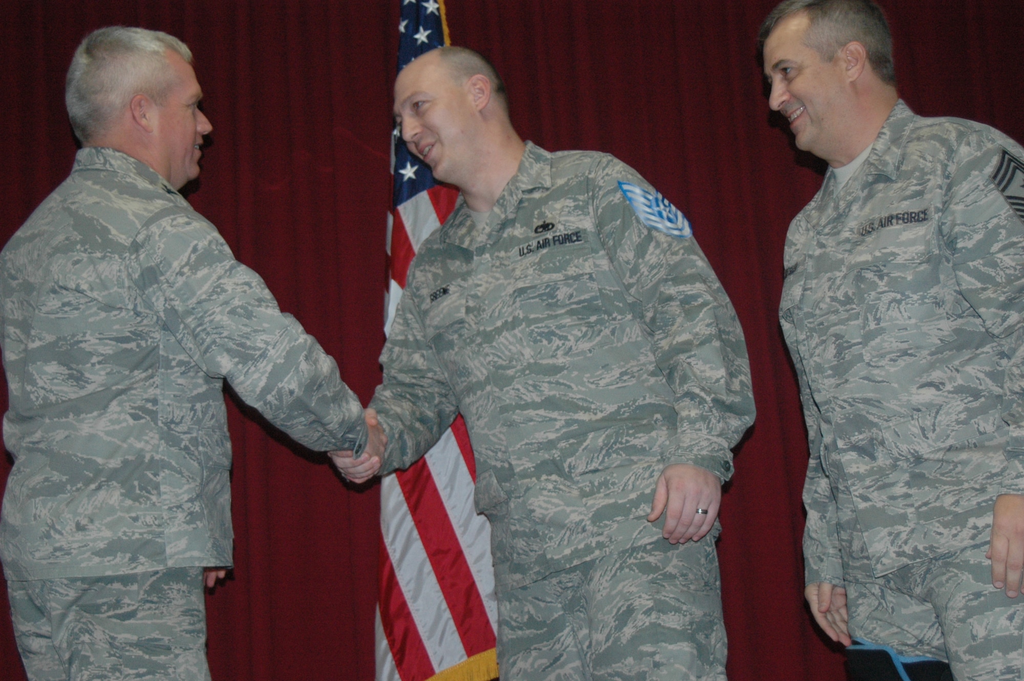 Col. Todd Harmer, 33rd Fighter Wing commander, congratulates Staff Sgt. Jeremy Greene, 33rd Maintenance Group quality assurance inspector, on promotion under the Stripes for Exceptional Performers program. After the surprise announcement was made during a Dec. 31 wing promotion ceremony, the NCO joined the commander and wing command chief, Chief Master Sgt. Douglas Kesler, right, on stage for the traditional recognition. (U.S. Air Force photo/Senior Airman Brian Miles)