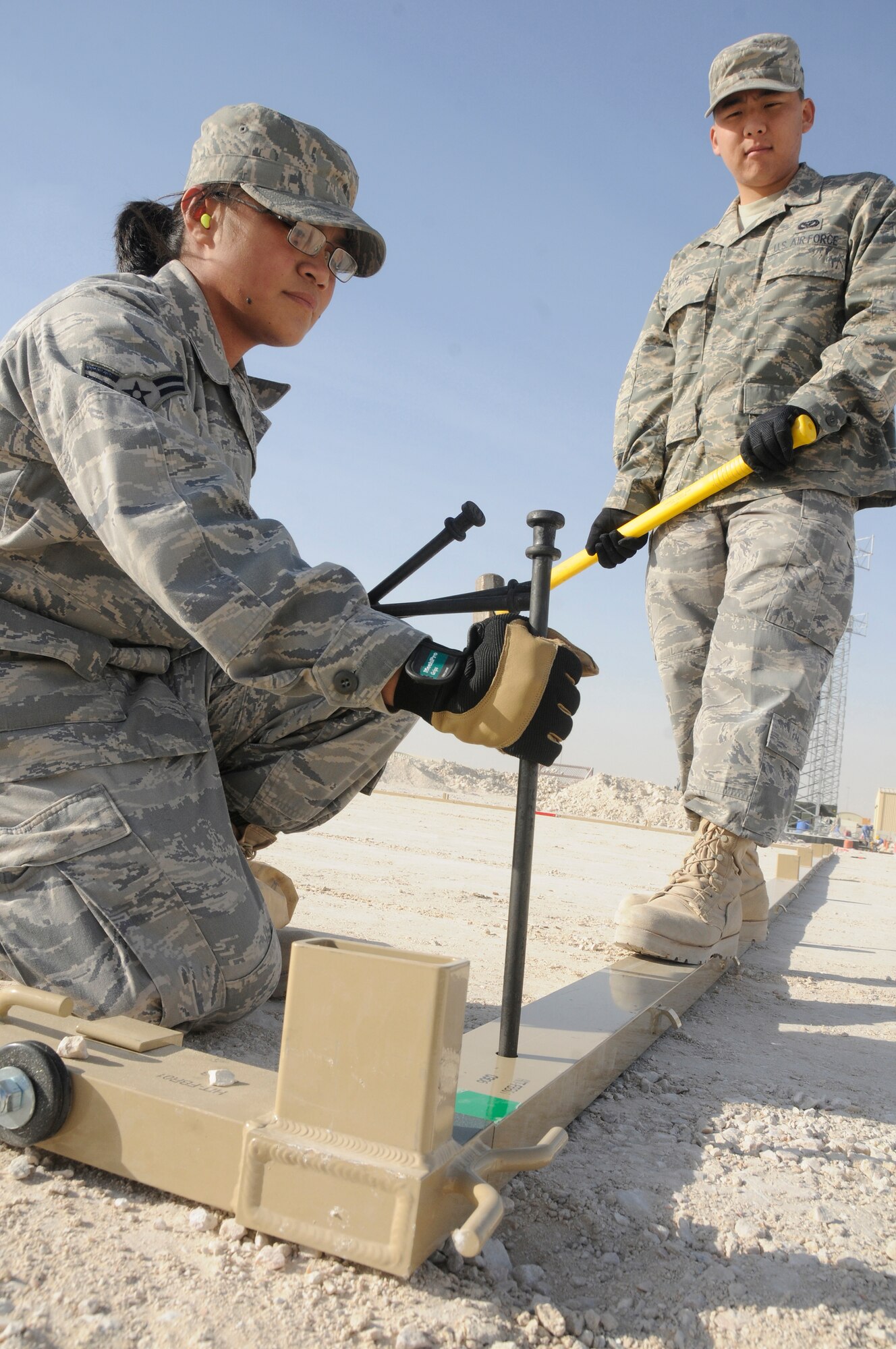 Airman 1st Class Ingrid Tomayo, holds a stake in place while Airman 1st Class Seung Kim prepares to drive the stake into the ground to hold a frame in place Jan. 2, 2009, at an undisclosed air base in Southwest Asia. Both Airmen are structural apprentices assigned to the 379th Expeditionary Civil Engineer Squadron, and are securing the base of a California tent.  These members are responsible for helping the base make the transition from expeditionary to enduring by creating new facilities. Airman Tomayo, a native of Los Angeles, Calif., and Airman Kim, a native of San Jose, Calif., both deployed from Travis Air Force Base, Calif.  Both are deployed in support of Operations Iraqi and Enduring Freedom and Joint Task Force-Horn of Africa. (U.S. Air Force photo by Staff Sgt. Darnell T. Cannady/Released)