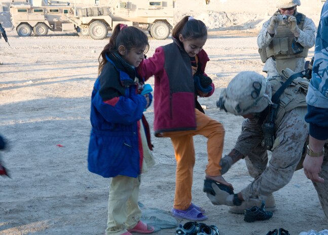 Lance Cpl. Derek Nelson, a 21-year-old team leader from Chino Hills, Ca., with 2nd Platoon, C Company, Task Force 1st Battalion, 3rd Marine Regiment, Regimental Combat Team 1, helps a young girl try on pairs of shoes. Marines trained for urban warfare performed a completely unrelated task at a clothing drive distributing winter coats and shoes to children in Karmah, Iraq, Jan. 6.