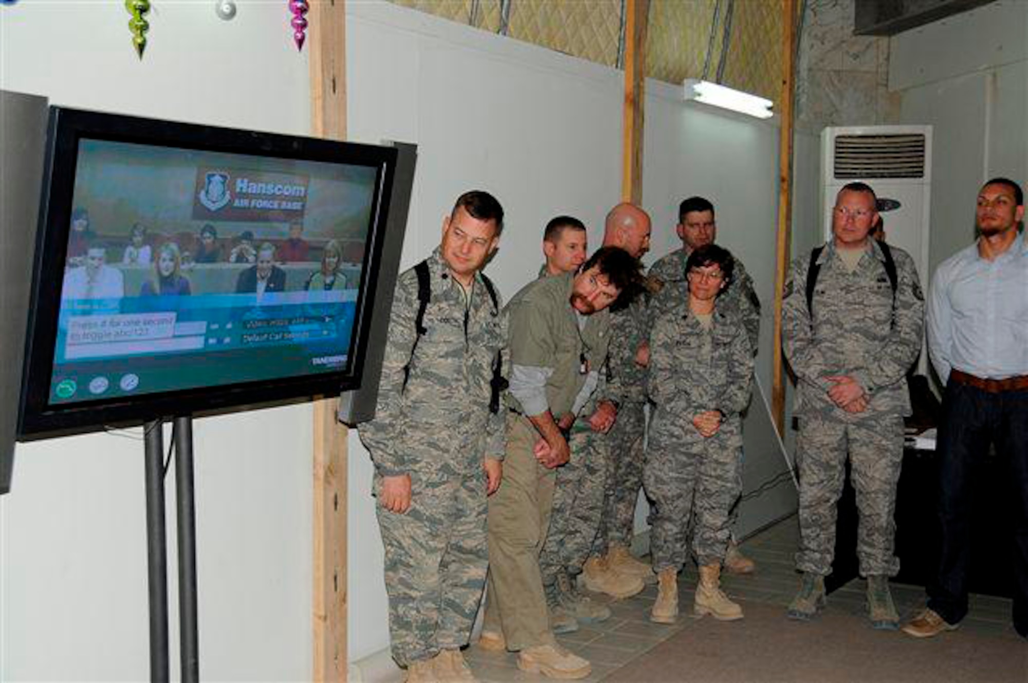 Maj. Ryan Robinson's friends and colleagues in Iraq watch the video monitor showing Major Robinson's family seated in Hanscom's video teleconference center prior to the promotion ceremony, held Dec. 30.  (Photo courtesy of the U.S. Air Force)