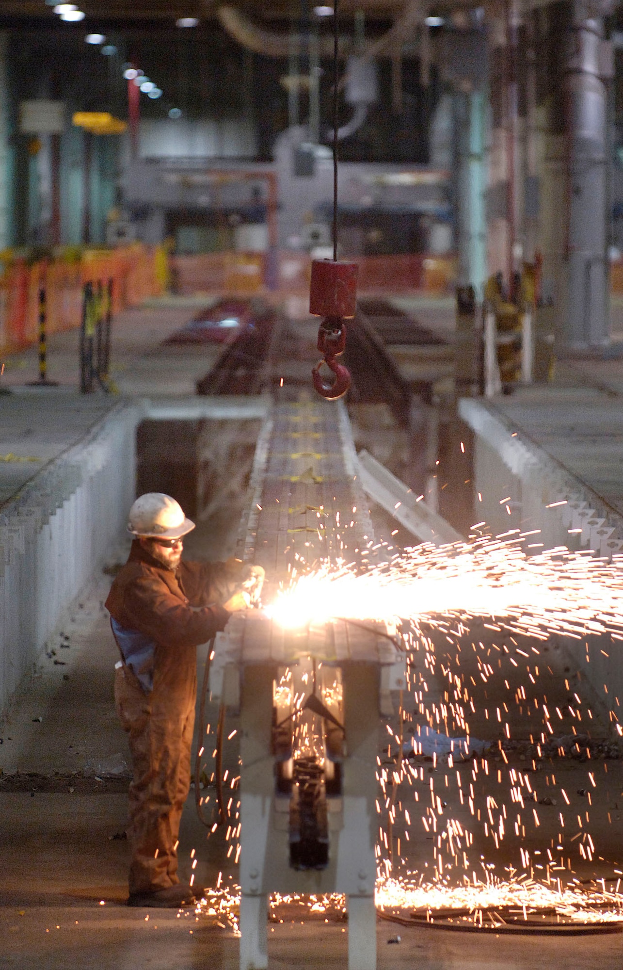 Tinker welder Jeff Tabor cuts through a section of a General Motors automobile final conveyor line at the Tinker Aerospace Complex recently while a waiting crane and other Tinker personnel will lift it from the pit.  Work continues to remove floor and overhead steel and other remnants of the GM plant to transform the cavernous building for Tinker’s work.  The area shown will eventually hold the sheet metal back shop now housed in Bldg. 2101. (Air Force photo/Margo Wright)
