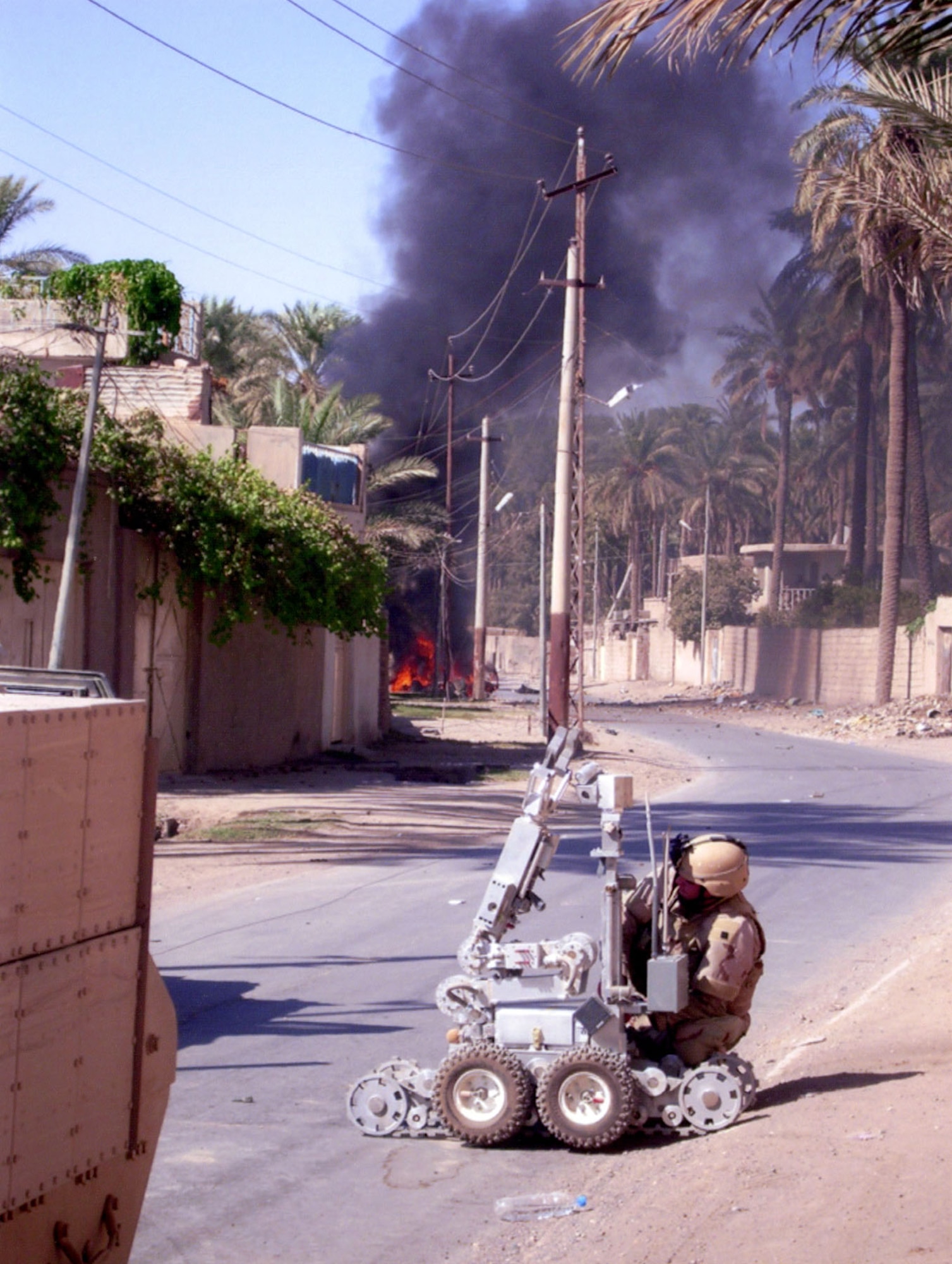 Senior Airman Kyle Preece shown working on an F6A robot as a vehicle borne IED burns in the background. (U.S. Air Force photo)