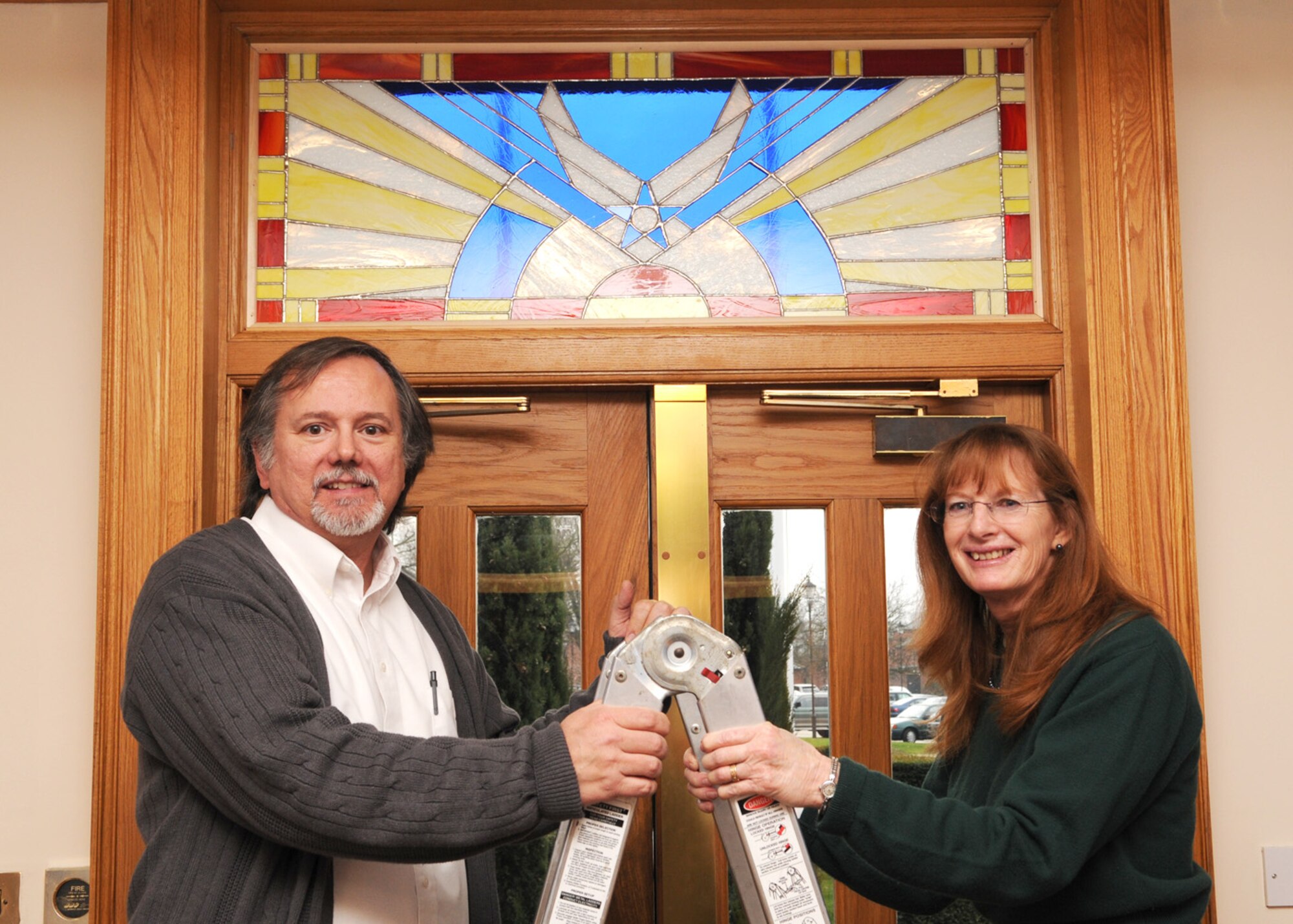 John P. Williamson, 100th Air Refueling Wing historian, and his wife Marguerite unveil a leaded glass window at the entrance of Building 239, the 100th ARW headquarters Jan. 7, 2009, in RAF Mildenhall, England. Mrs. Williamson has worked on the piece for more than 10 months, dedicating it to the U.S. Air Force and the Royal Air Force for selfless service. The piece encompasses the Royal Air Force symbol at the bottom portion while the United States Air Force symbol sits just above it. (U.S. Air Force photo by Staff Sgt. Jerry Fleshman)