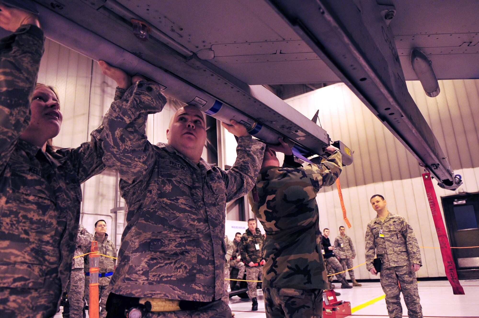 Senior Airman Billy Peacock, Senior Airman Athena Keller, and Staff Sgt. Matthew Fratzke, Weapons Load Team Chief, all from the 354th Aircraft Maintenance Squadron load an AIM-9L/M Sidewinder Missile during a load competition. The competition was judged based on the speed a weapon could be loaded while following a list of technical orders, and also maintaining safety. (U.S. Air Force photo/Airman 1st Class Willard E. Grande II)