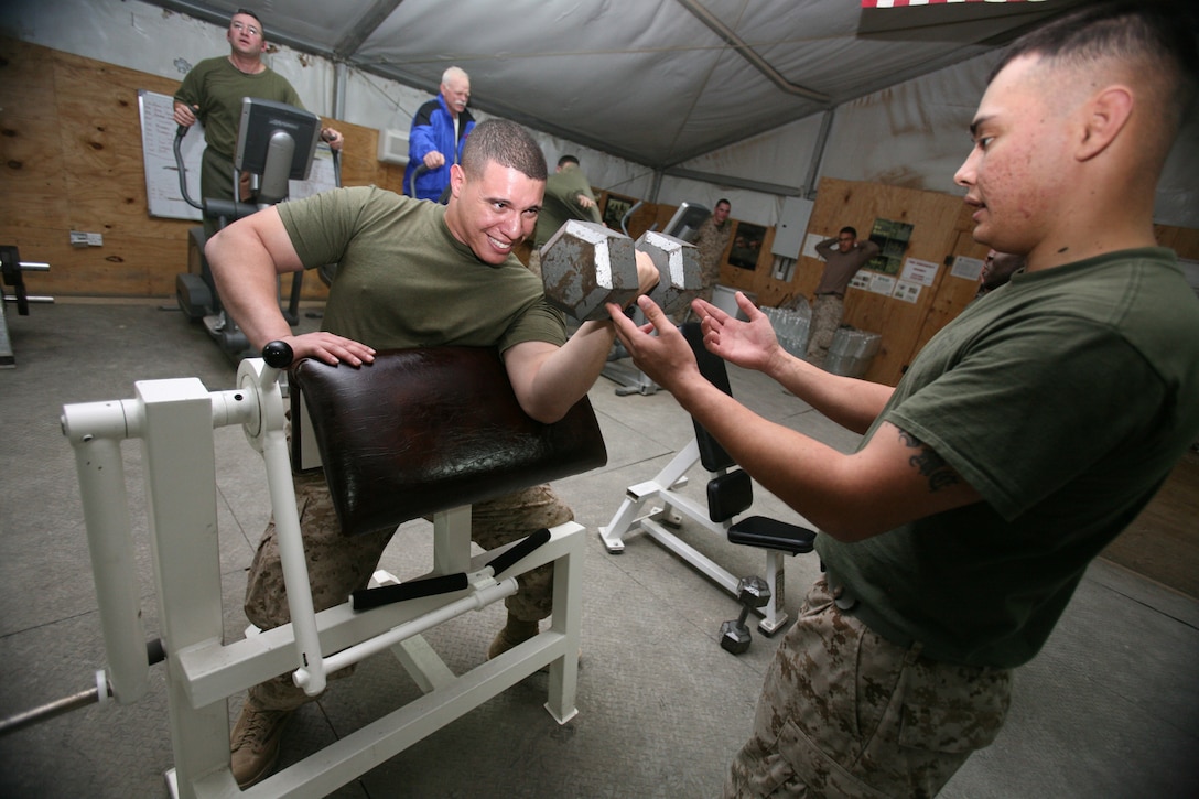 Lance Cpl. Mark Unpingco (right), a maintenance management specialist, assists Cpl. David Olivier, also a maintenance management specialist with Headquarters Company, Regimental Combat Team 8 at the gym here. Marines with RCT-8 are able to use the gym day or night, being able to fit physical exercise into their daily regimen while deployed. (Official U.S. Marine Corps photo by Cpl. Eric C. Schwartz)