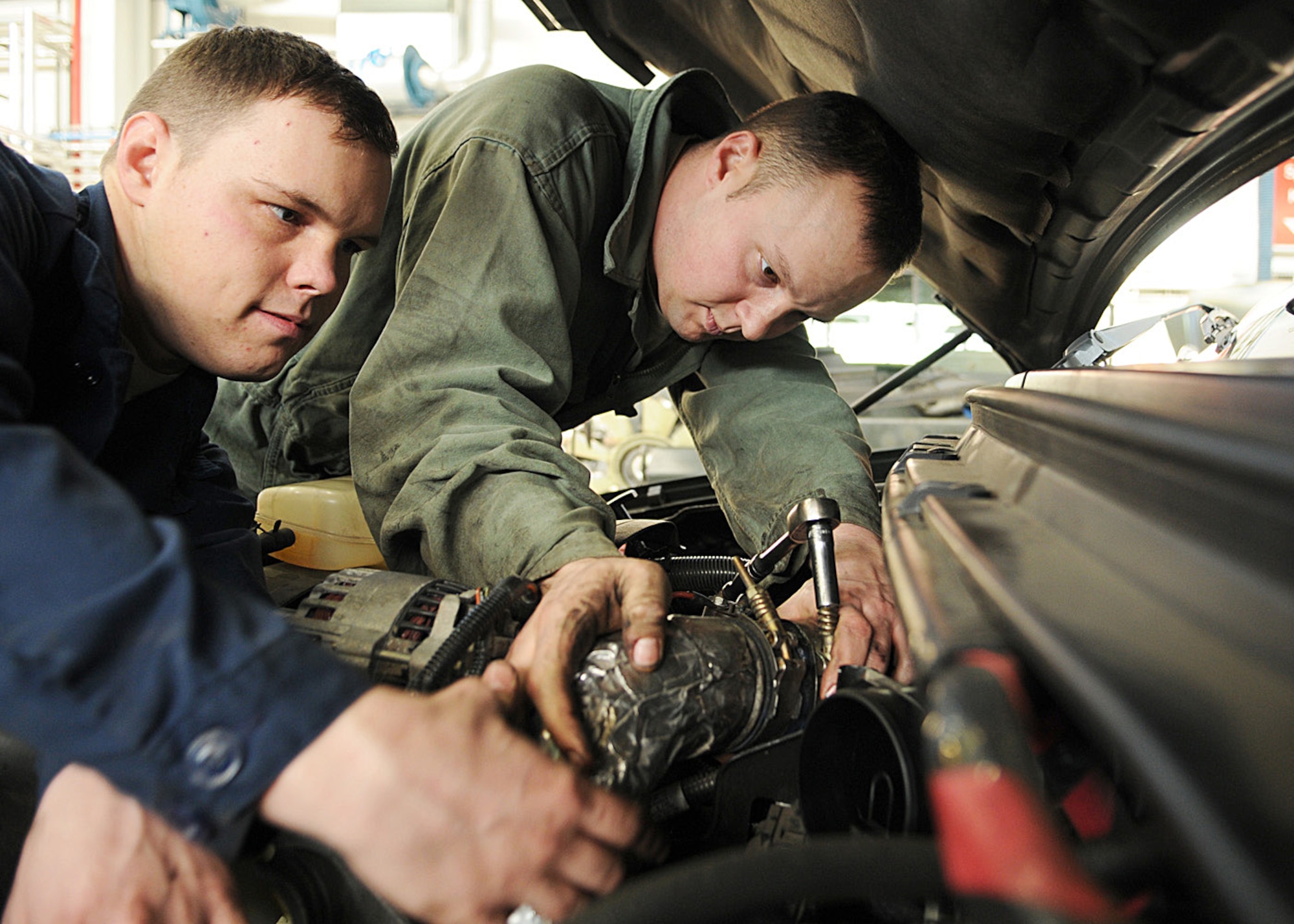 Staff Sgt. Justin Creel, in green coveralls, and Airman 1st Class Timothy Reuwer. both 100th Logistics Readiness Squadron vehicle maintenance technicians, tighten a clamp after repairing a power steering pump leak here Dec. 18, 2008, at RAF Mildenhall, England. (U.S. Air Force photo by Staff Sgt. Jerry Fleshman) 