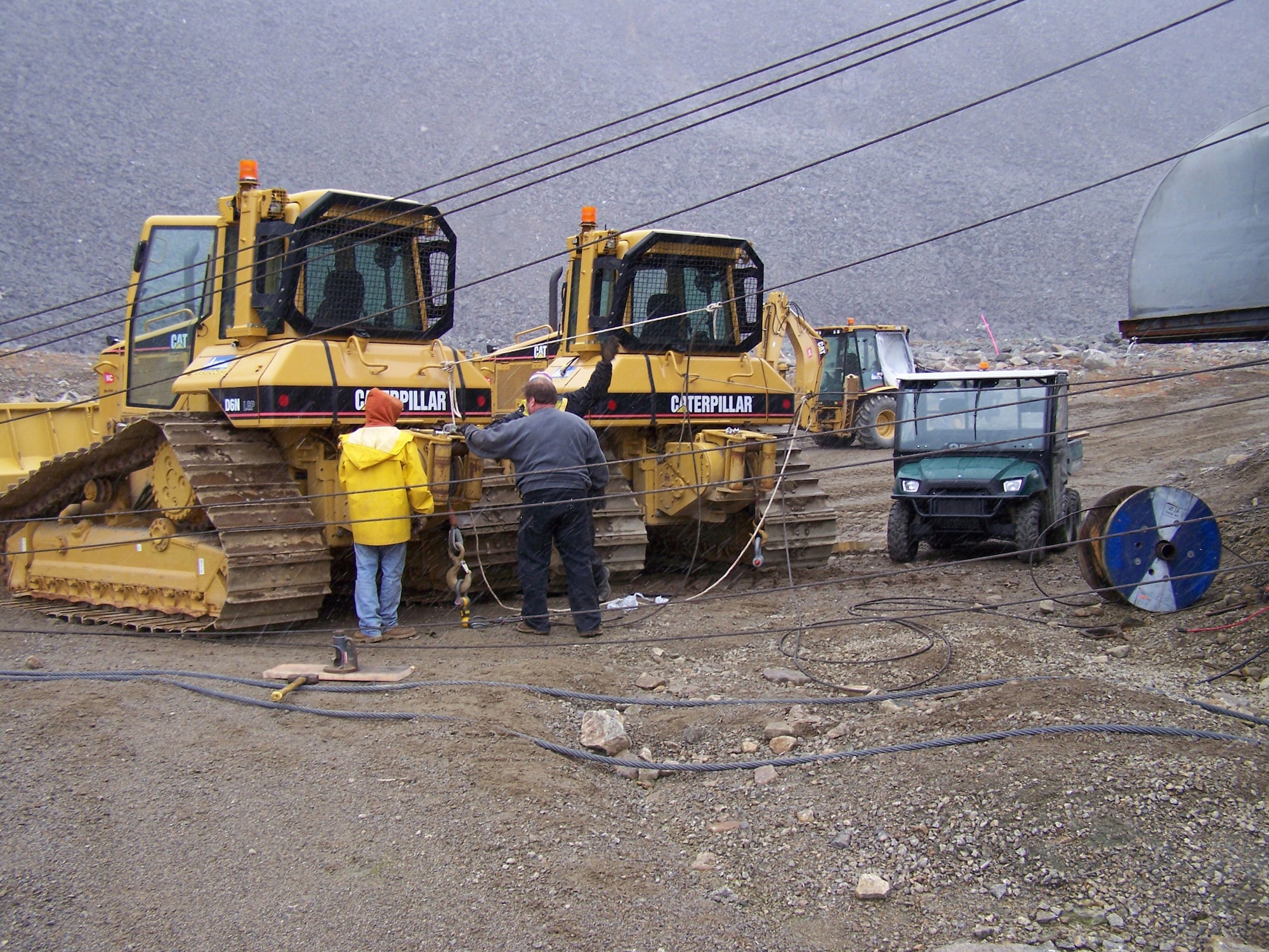 Dave Kerns, facilities maintenance specialist, left, and Denny Hodges, aerial tram specialist, inspect cable riggings prior to a 14 ton pull of the aerial tram at Cape Romanzof Long Range Radar Station. The tram connects the upper and lower camps. Both the tram and a road are used by the employees to access the upper camp depending on weather conditions and the work required.