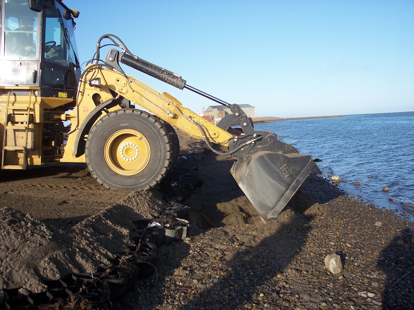 An ARCTEC employee spreads dirt and gravel over geo-web material as he repairs the ?toe? area along the seawall which protects the airfield at Barter Island Long Range Radar Station.