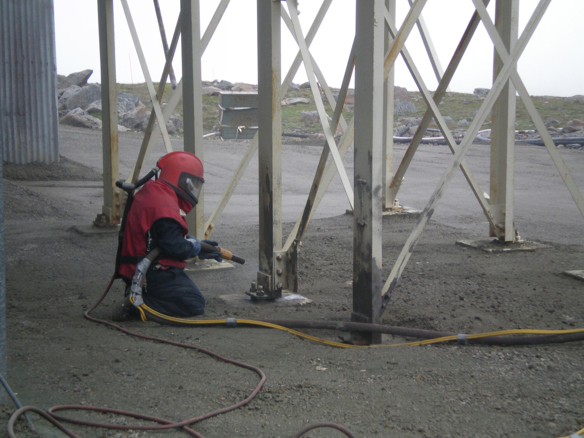Max Whittaker, facilities specialist, wears safety equipment as he ?sandblasts? the lower aerial tram building structural steel supports at Cape Romanzof Long Range Radar Station. Corrosion control at the coastal radar sites is important due to the saltwater environment.     