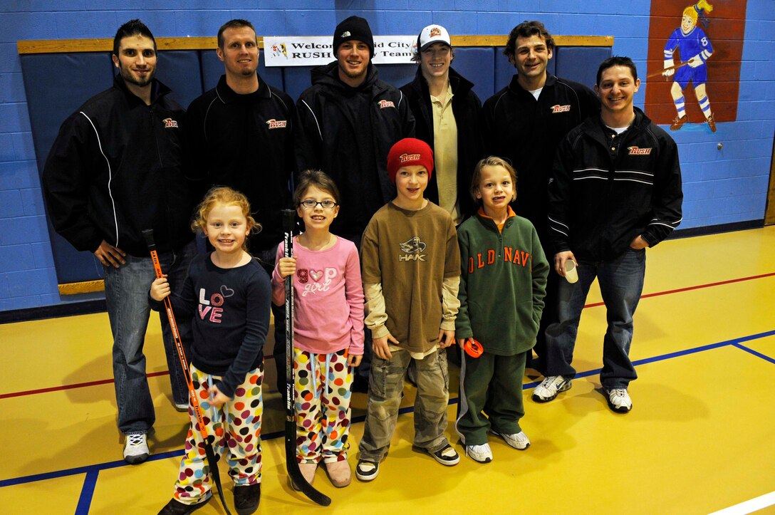 (Front row from left to right) Sage Nicolaisen, Erin Nicolaisen, Wyatt Hunt, and Dominic Nicolaisen have a photo taken with six stars from the Rapid City Rush hockey team at the Youth Center here, Jan. 15. Members of the team signed posters, sticks, and pucks for the kids. (US Air Force photo/Airman 1st Class Corey Hook)