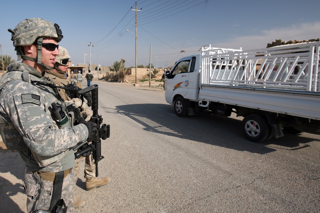 A psychological operations soldier with 320th Psychological Operations Company, Detachment 1243, and a Marine with Civil Affairs Team 5, Civil Affairs Group, Regimental Combat Team 8 stand on the side of the road as an Iraqi civilian vehicles passes along. According to the new status of forces agreement signed by the United States and Iraqi governments, coalition forces must pull over or move out of the way for vehicle traffic in Iraq. (Official U. S. Marine Corps photo by Cpl. Eric C. Schwartz)