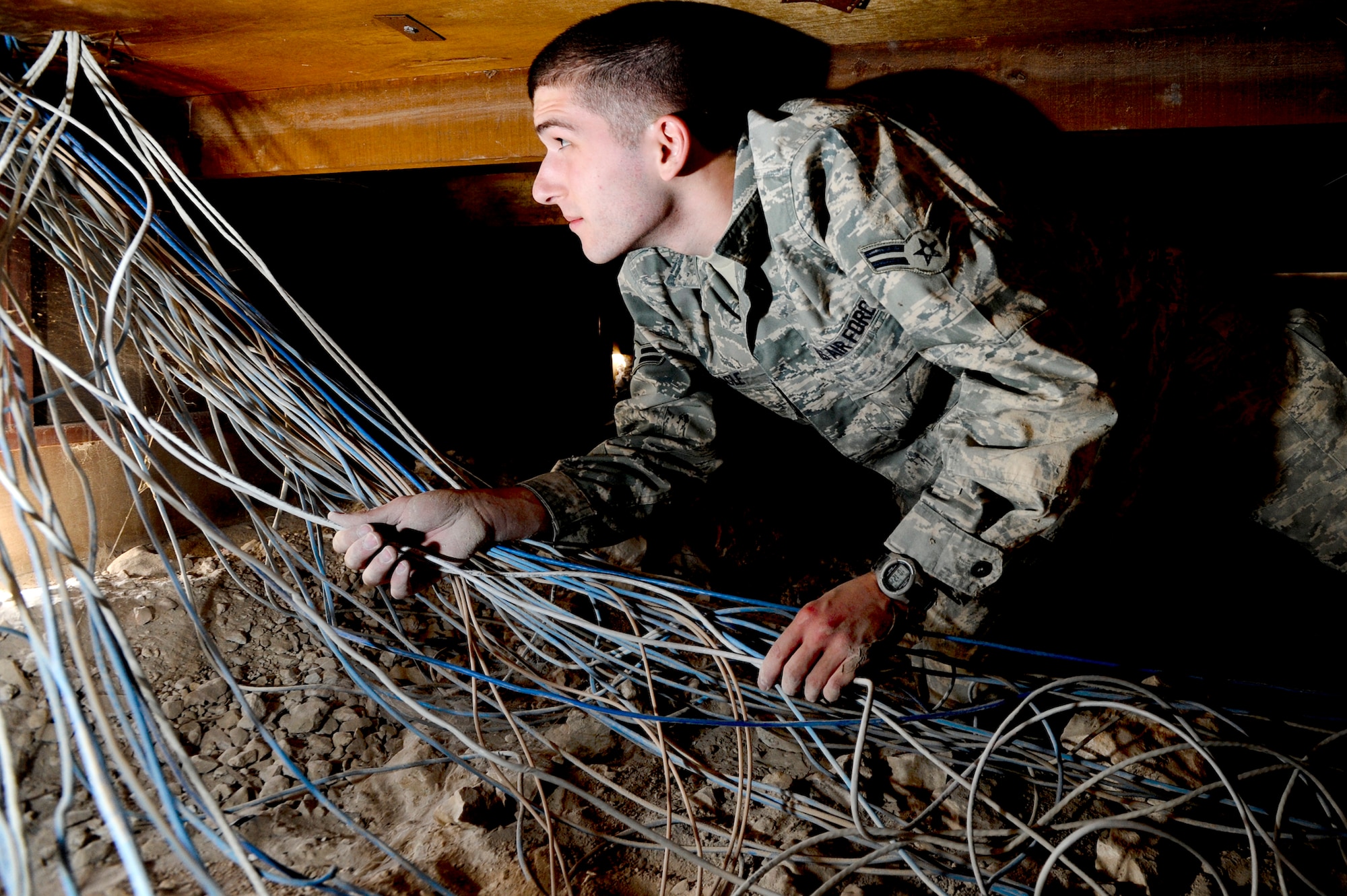 Airman 1st Class Uriah Beagle, a 379th Expeditionary Communication Squadron telephone maintenance technician, feeds category 5 (CAT5) wire to a communications room from under a compound building, Jan. 18, 2009, in an undisclosed location in Southwest Asia. Airman Beagle and fellow telephone maintenance technicians have to pull the CAT5 wire either through roofs, or underneath structures to ensure the base is completely LAN connected. Airman Beagle is originally from Bloomsburg, Pa. and is deployed from McChord Air Force Base, Wash. in support of Operations Iraqi and Enduring Freedom and Joint Task Force-Horn of Africa.  (U.S. Air Force Photo by Staff Sgt. Joshua Garcia/Released)