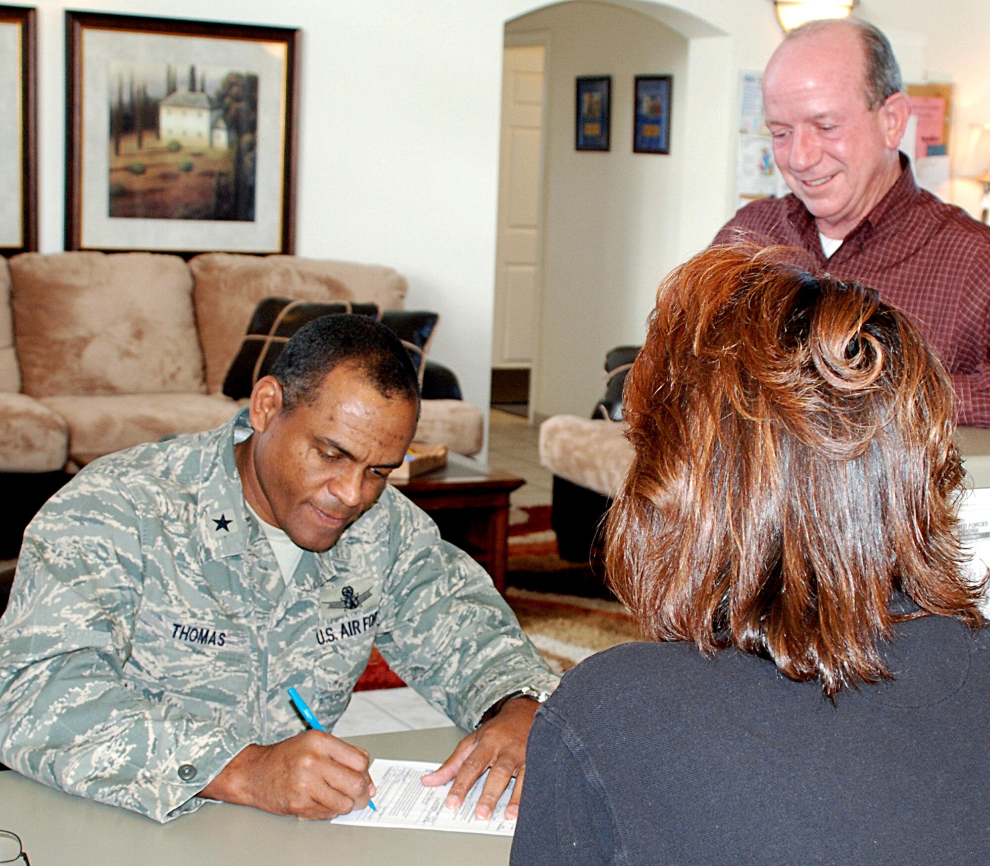 KIRTLAND AIR FORCE BASE, New Mexico -- Brig. Gen. Everett Thomas, Air Force Nuclear Weapons Center commander, completes his annual Basic Allowance for Housing update here. The form, provided by Kristi Wagner, Kirtland Family Housing, is required for active duty military base housing residents. Paul Tourne, KFH community director, right, said that this is the last year for this because housing is changing to a new system called Military Assistance Company which changes and updates BAH paperwork automatically. U.S. Air Force photo by Dennis Carlson