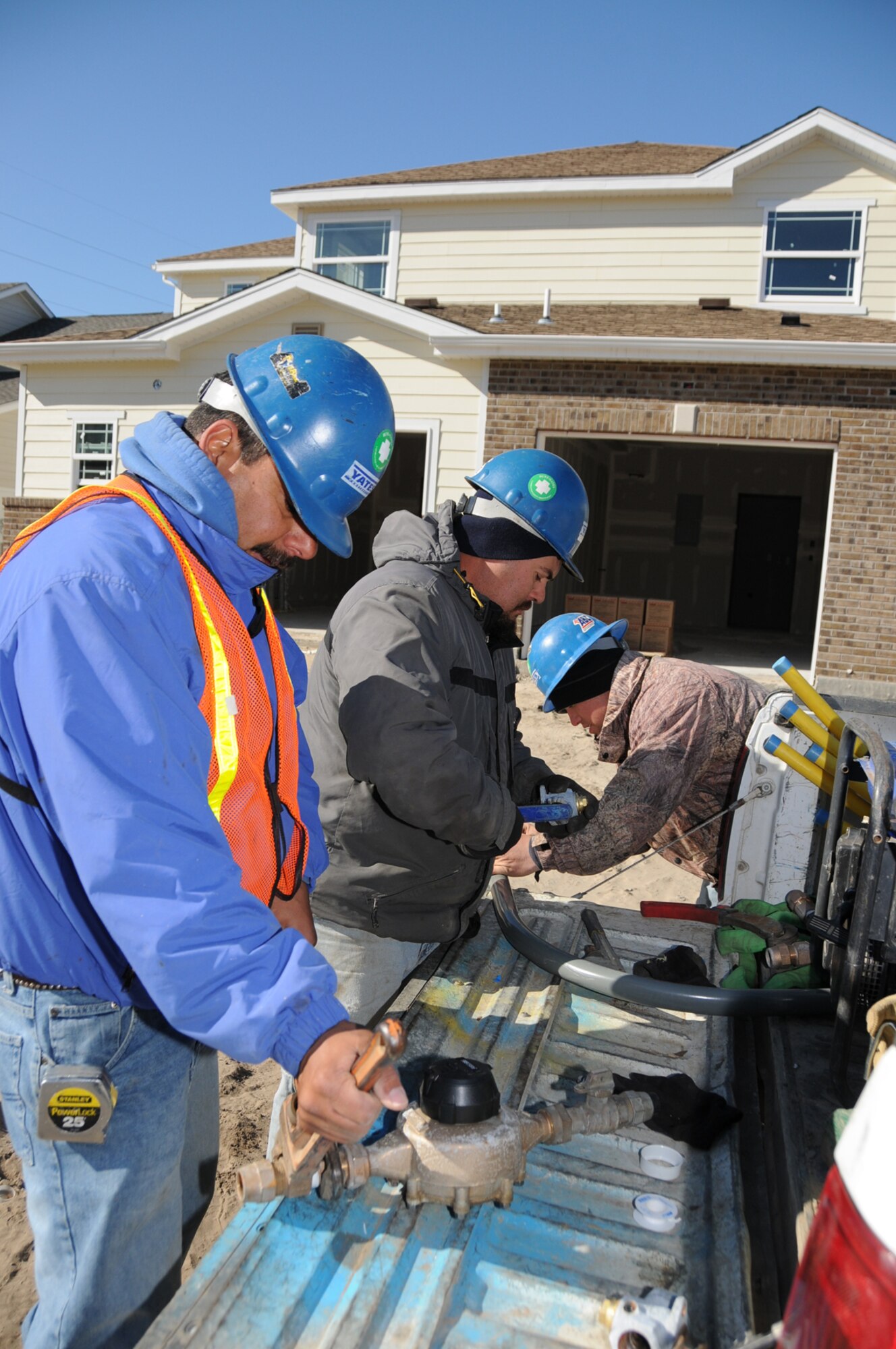 From left, pipefitters Juan Marta, Michael  Willard and Wallace Rogers prepare fittings for water meters and gas service installation for new homes Friday in West Falcon Park.  (U.S. Air Force photo by Kemberly Groue)