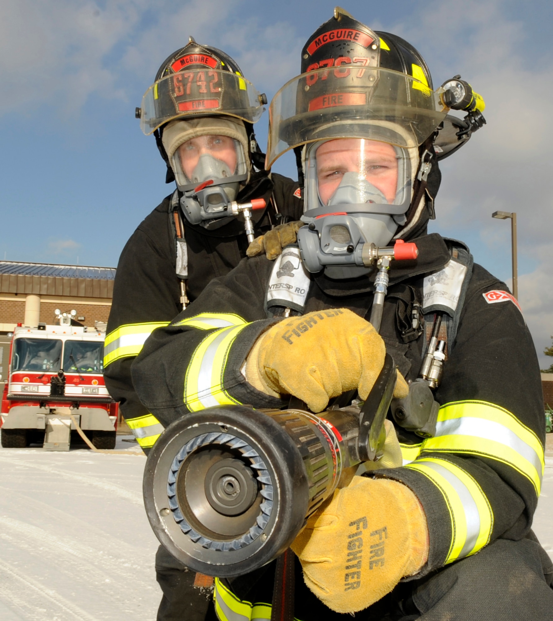 Right, Jeremy Bourquin, 305th Civil Engineer Squadron firefighter, simulates hand line operations during egress training exercises Jan. 15. The nozzle contains a pistol-like grip on the bottom for extra stability. The firefighter can control the water stream by pulling the top lever back. The gloves are worn year round and are fire resistant to help protect hands from injury. Left, Staff Sgt. Stephan Gallick, 514th CES Reservist, helps stabilize the hose line. The line pulls the firefighters back, due to the high water pressure, so his job is to pull the line forward. (U.S. Air force photo/Carlos Cintron) 