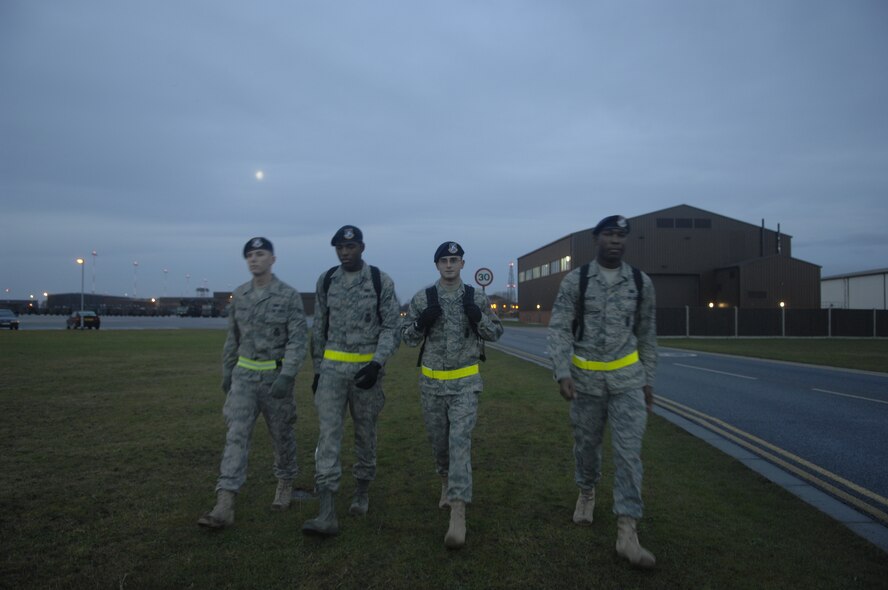Airmen 1st Class John Foreman, Michael Bradley, Michael Pradella and Delmario Carson from the 100th Security Forces Squadron, make their way to work Tuesday.  The wear of a reflective belt is required for all Airmen during limited visibility. The Airmen have all just arrived to RAF Mildenhall and are currently in Phase I Security Forces familiarization training. The training provides Security Forces Airmen with a base orientation to include gate and flightline security. (U.S. Air Force Photo by Master Sgt. Charles Tubbs)
