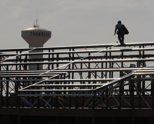 Raul Corona, Alert Roof Systems roofer, contractors of Cram Roofing, catches a panel clip from fellow co-worker Humberto Tadeo on the roof tops of dorm building 637 recently.  (US Air Force photo/Airman 1st Class Ronifel Yasay)