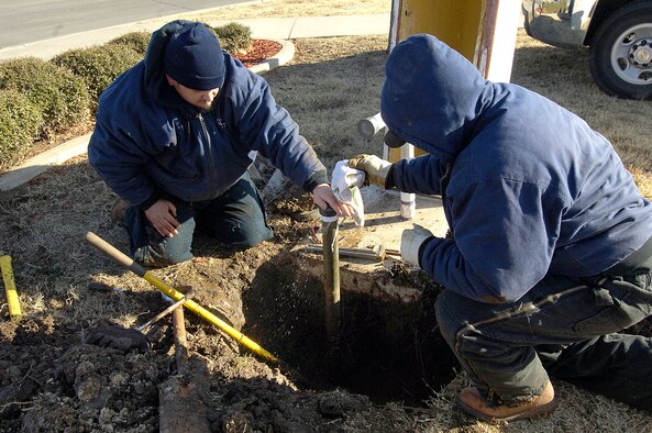 Tinker exterior plumbers Jack Hasha, left, and David Black repair a leaky sprinkler system near the intersection of Arnold Street and Air Depot on a day when the sun can’t discourage 25 degree highs and a steady wind. Temporary water spray is stopped by bare hands and a cloth after water-soaked gloves became useless against the cold and instead froze to metal tools. A nearby idling truck’s heated cab offered a welcome shelter for a break. (Air Force photo/Margo Wright)