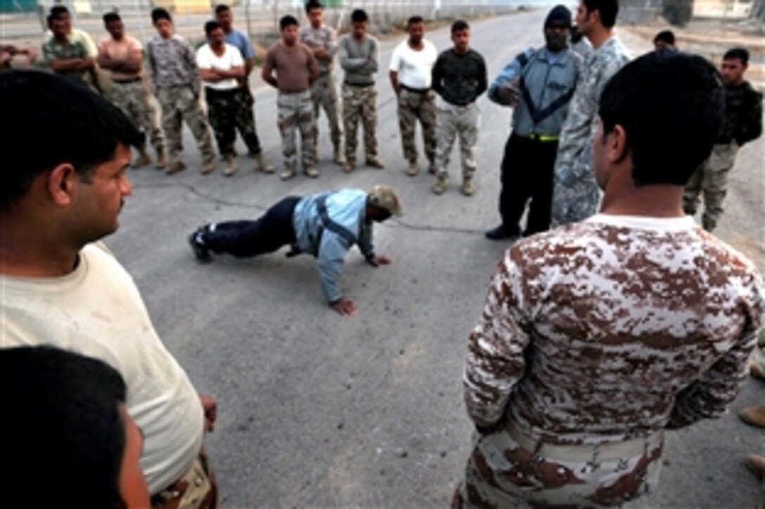 A U.S. soldier from the 25th Infantry Division's 2nd Stryker Brigade Combat Team  demonstrates a proper push-up to Iraqi soldiers during a physical fitness test on Camp Taji, Iraq, Jan. 11, 2009.