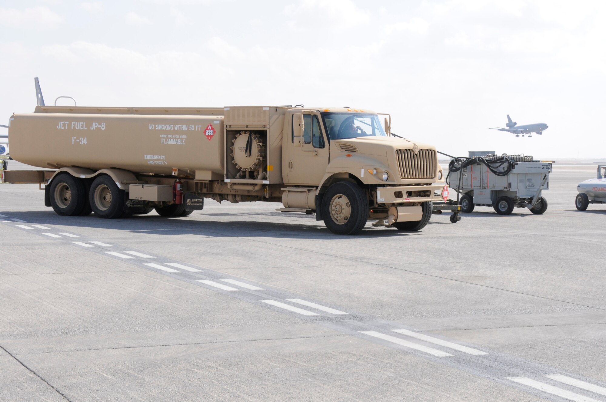 SOUTHWEST ASIA -- A KC-10 Extender comes in for a landing while Airman 1st Class Brian Holley, 380th Expeditionary Logistics Readiness Squadron fuels operator waits to be ushered in to refuel an E-3 Sentry, Jan 21. Airman Holley is behind the wheel of an R-11 fuels truck which holds 6,000 gallons of fuel. The E-3 Sentry takes 20,000 gallons to refuel when completely empty. Airman Holley is deployed from the 178th Fighter Wing, Ohio Air National Guard and is from Dayton, OH. (U.S. Air Force photo by Senior Airman Brian J. Ellis) (Released)