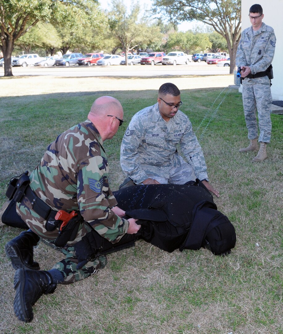 Tech. Sgt. Karl Killebrew (kneeling left), 12th Security Forces Squadron, and XXXX, 12th Medical Group, assist Staff Sgt. Mike Trejo (in protective suit), as he goes down during TASER training Jan. 20 outside the security forces complex. (U.S. Air Force photo by Rich McFadden)