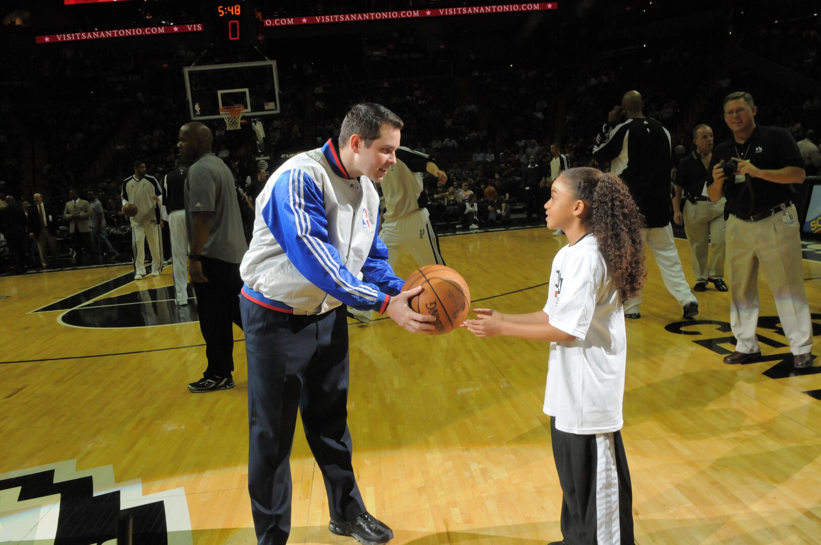 Anissa Sidney, daughter of Tech. Sgt. Marcus Sidney, 12th Security Forces Squadron, passes the official game ball to an official just before tip-off of the Spurs-Nets game on military appreciation night Jan. 23. In addition to being the honorary ball-girl for the game, Anissa's father appeared on the Jumbotron from his deployed location to say hello and deliver an inspiration message to his daughter and wife, Tech. Sgt. Vanessa Sidney. (U.S. Air Force photo by Melissa Peterson)