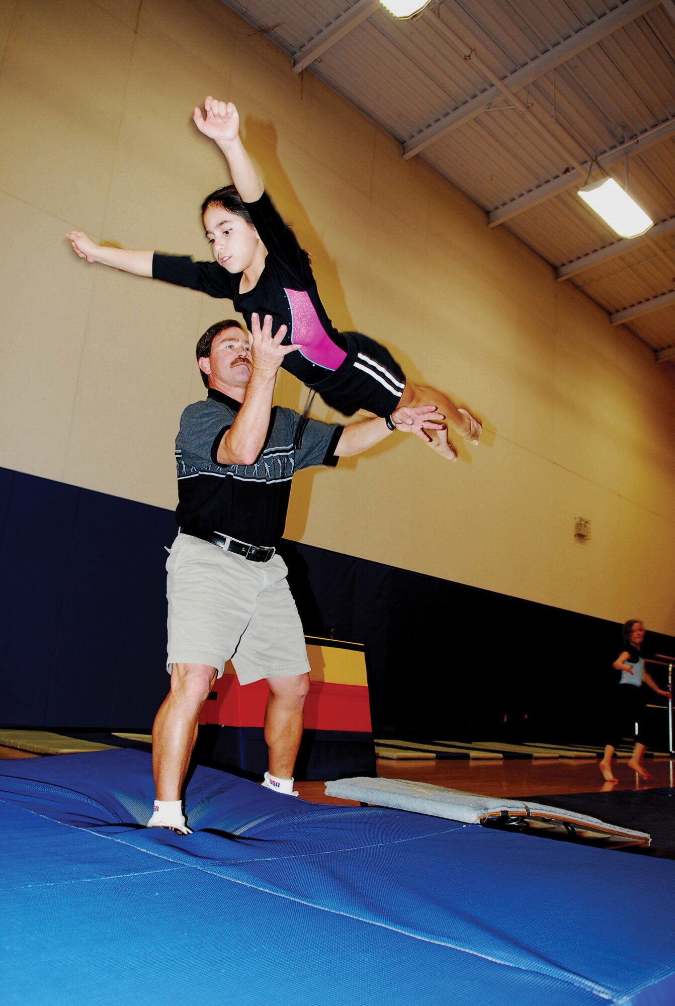Cliff McGonolis, gymnast instructor, helps Sofia Barajas, 9, with a dive roll during gymnastics Monday. Gymnastics is one of the many programs offered at the youth center. For more information about programs and activities, call the youth center at
(623) 856-6225.