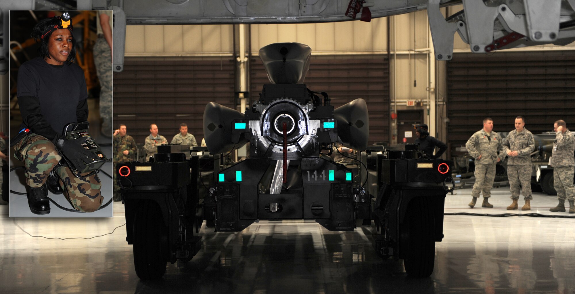 WHITEMAN AIR FORCE BASE, Mo. - Senior Airman Eleasha Holmes, 509th Bomb Wing Munitions Squadron, guides in the conventional rotary launch assembly with four by Air to Ground Missile 158s non-flying under the Weapons Load Trainer a B-2 mock up, the weapons load trainer, 21 Jan. Holmes is competing in Giant Sword Two a weapons loading and career knowledge competition being conducted on five bases around the United States. Inset Photo: Airman Holmes, operates the control box to the conventional rotary launch assembly loader Jan 21. She uses this control box to make minor adjustments to the assembly to make sure it sits correctly in the weapons load trainer for a proper fit. (U.S. Air Force Illustration by Airman 1st Class Carlin Leslie)