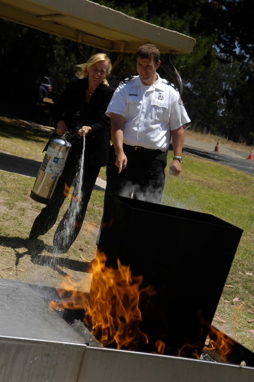 VANDENBERG AIR FORCE BASE, Calif. -- Lori Redhair, a 30th Space Wing contractor, puts out flames with the help of fire inspector Scott Balatgek on a fire extinguisher simulator July 1. The 30th SW Safety Office held the 2009 Safety Day Event at Cocheo Park here with safety displays, static display emergency vehicles and hands-on fire safety training.  (U.S. Air Force photo/Staff Sgt. Vanessa Valentine)