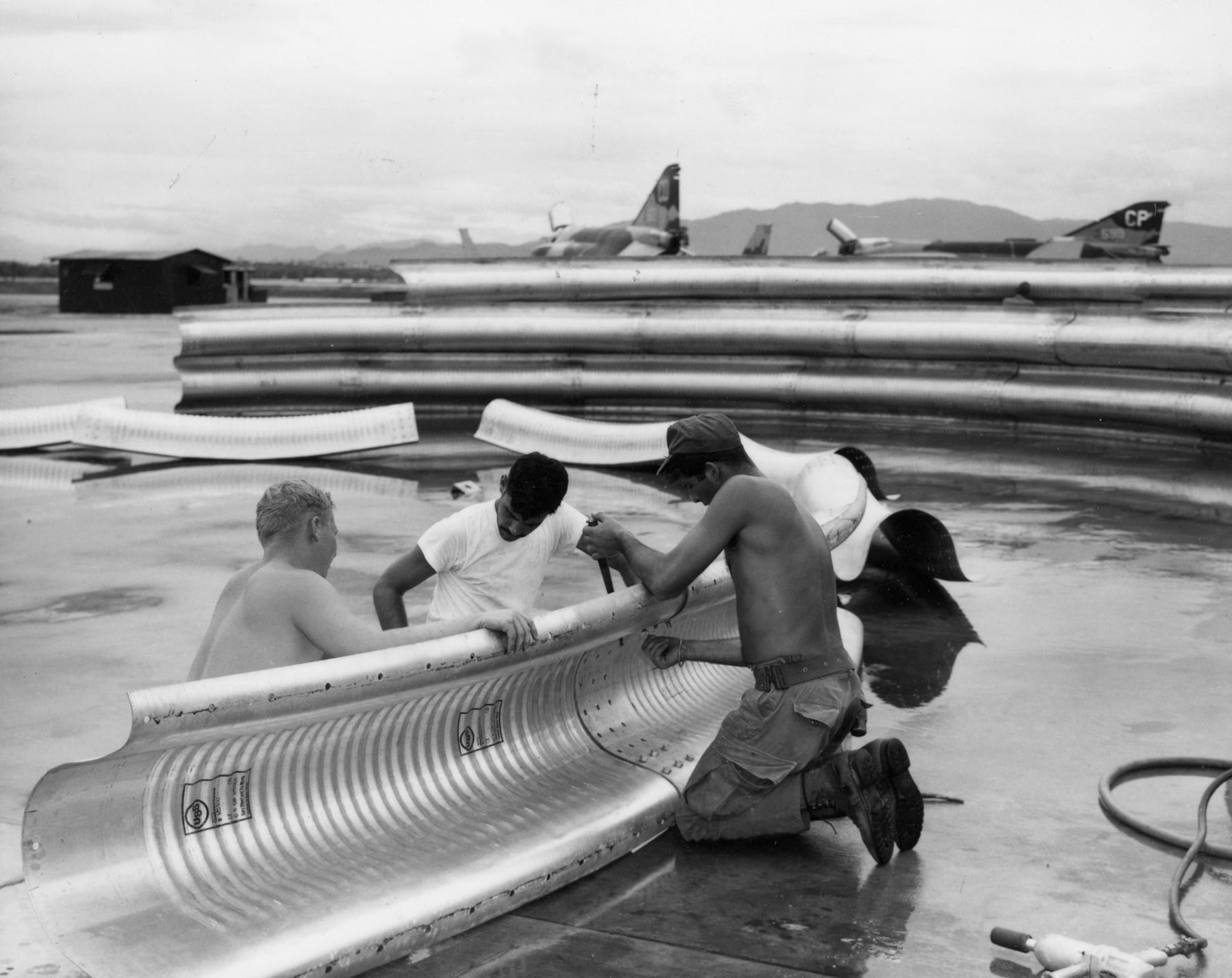 Three members of the 820th Civil Engineering Squadron RED HORSE belt together panels of galvanized steel to make one arch for an aircraft shelter being constructed at Da Nang AB, South Vietnam, in October 1968. (U.S. Air Force photo)