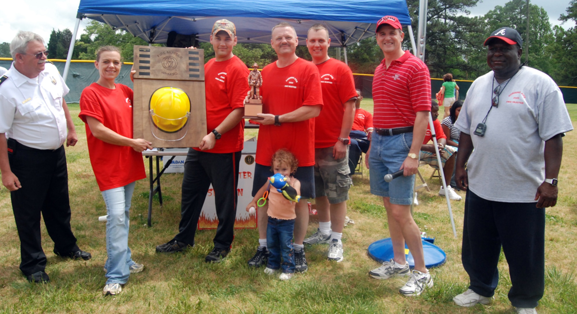 (Left to right in red shirts) 94th Aeromedical Staging Squadron members Master Sgt. Cynthia Anderson, Senior Airman Matthew Davis, Capt. Darryl Blalock and Staff Sgt. Joshua Bense are presented trophies as the overall winners of the Fire Muster at the annual Family Day May 2. The yellow helmet trophy is called the roving trophy, which units hold onto until the next year's competition.  The bronze trophy is awarded as being the winner for the year. 