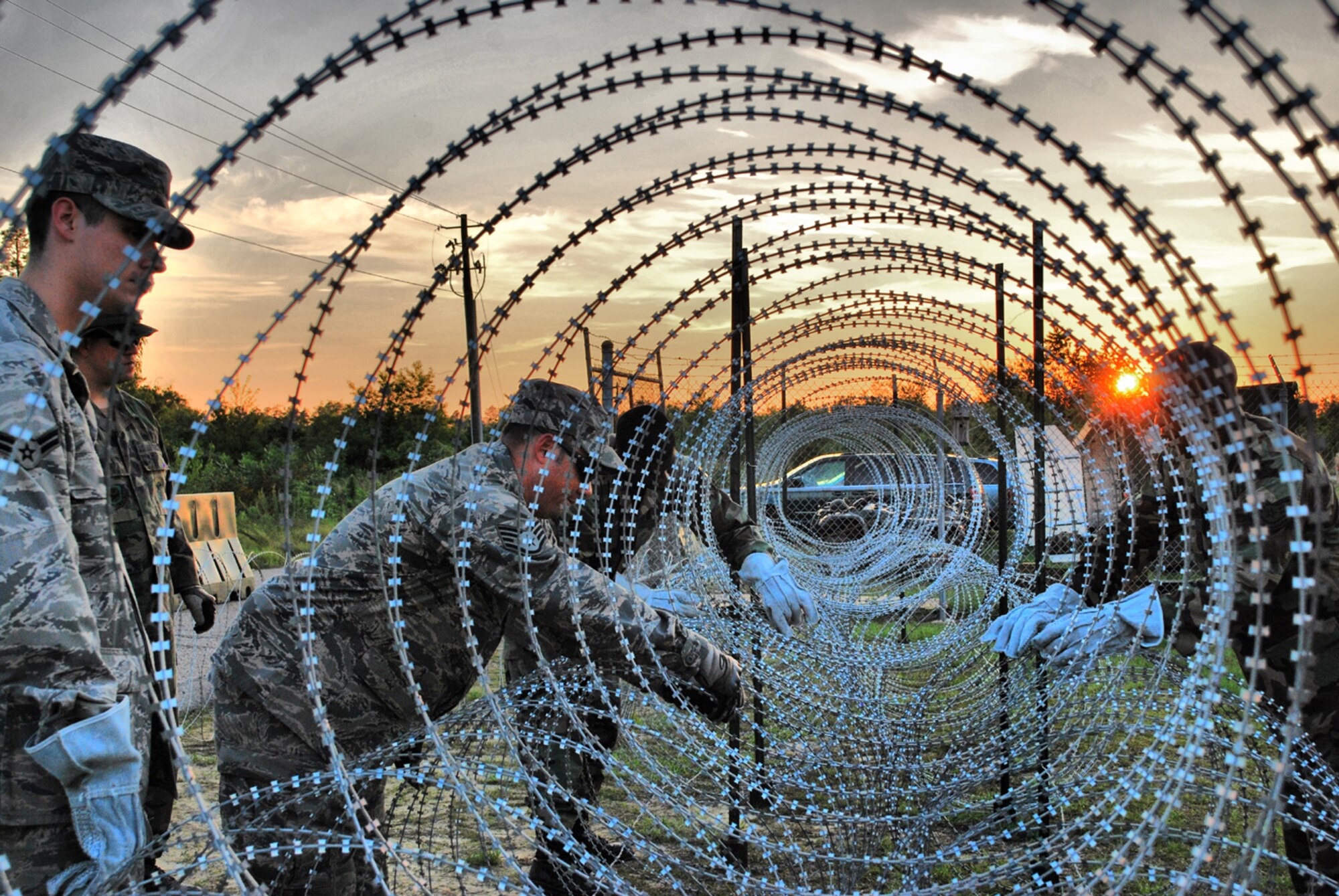 Airmen from the 621st Contingency Response Wing construct razor wire fences around their camp perimeter during a noncombatant evacuation exercise at Mackall Army Airfield, N.C., June 22-26. While the exercise scenario started peacefully in the fictional African country of Chatu, CRW Airmen set-up perimeter defenses and manned defensive fighting positions as the situation became hostile. After paratroopers from the Army's 82nd Airborne Division jumped in to provide support and escort American citizens to the airfield, CRW Airmen loaded more than 1,000 passengers and 40 short tons of cargo onto C-17 and C-130 aircraft for evacuation. (U.S. Air Force photo/Staff Sgt. Nicholas Phelps)