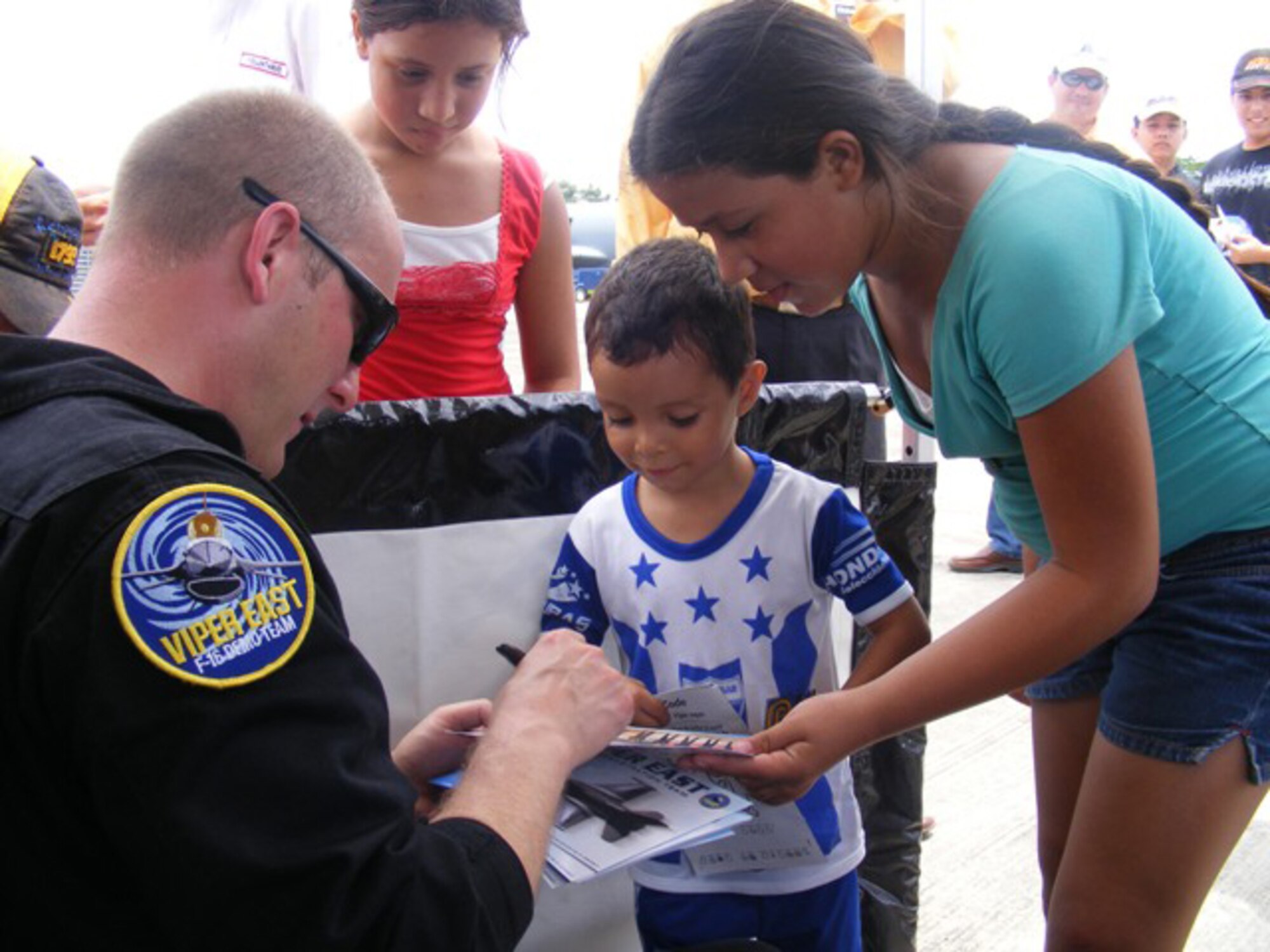 Master Sgt. Bryan Spangler, Viper East F-16 Demo Team Chief, signs an autograph for a Honduran boy at an air show here June 20. More than 30 Airmen participated at the international air show June 20-21. The more than $35,000 proceeds from the show will help build a children?s intensive care unit at a local hospital. 