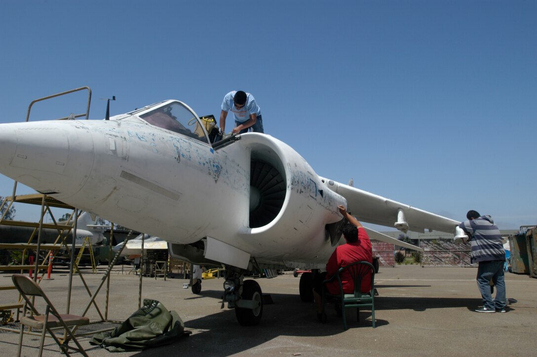 Volunteers with the Hire-A-Youth summer employment program sand the body of one of the Marine Corps' first four AV-8A Harriers July 2, 2009, to prepare it for repainting at the Marine Corps Air Station in Miramar, Calif. Miramar's Flying Leatherneck Aviation Museum plans to repaint the Hawker Siddeley-built Harrier with the original paint scheme from April 16, 1971, when it was first delivered to Marine Attack Squadron 513, then based in Beaufort, S.C., and now based in Yuma, Ariz. Restoration is expected to be completed by October, and it will be placed on display at the museum, said George Welsh, museum archivist. VMA-513 was the first Marine squadron to transition to the Harrier. After moving to Yuma in 1976, the Flying Nightmares used the plane until Jan. 21, 1986, when it was given to NASA where it was modified as an AV-8C and used to test wing design. The museum obtained the Harrier in 2008. (Photo by Gunnery Sgt. Bill Lisbon)