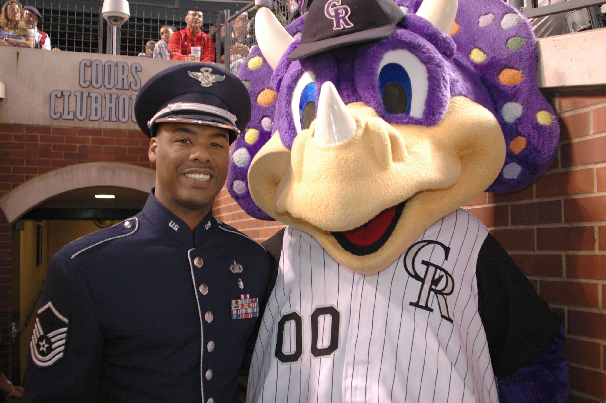Master Sgt. Aaron Miles, a vocalist with the Air Force Reserve Command Band, has his photo taken with "Dinger the Dinosaur" July 4 at Coors Field in Denver. Sergeant Miles set a patriotic tone by presenting the National Anthem to more than 51,000 fans, and during the game?s seventh-inning stretch, he sang God Bless America to the roaring crowd in celebration of Independence Day. Coors Field is home to the Major League Baseball's Colorado Rockies. Dinger the Dinosaur is the team?s mascot. (U.S. Air Force photo/Ann Skarban)