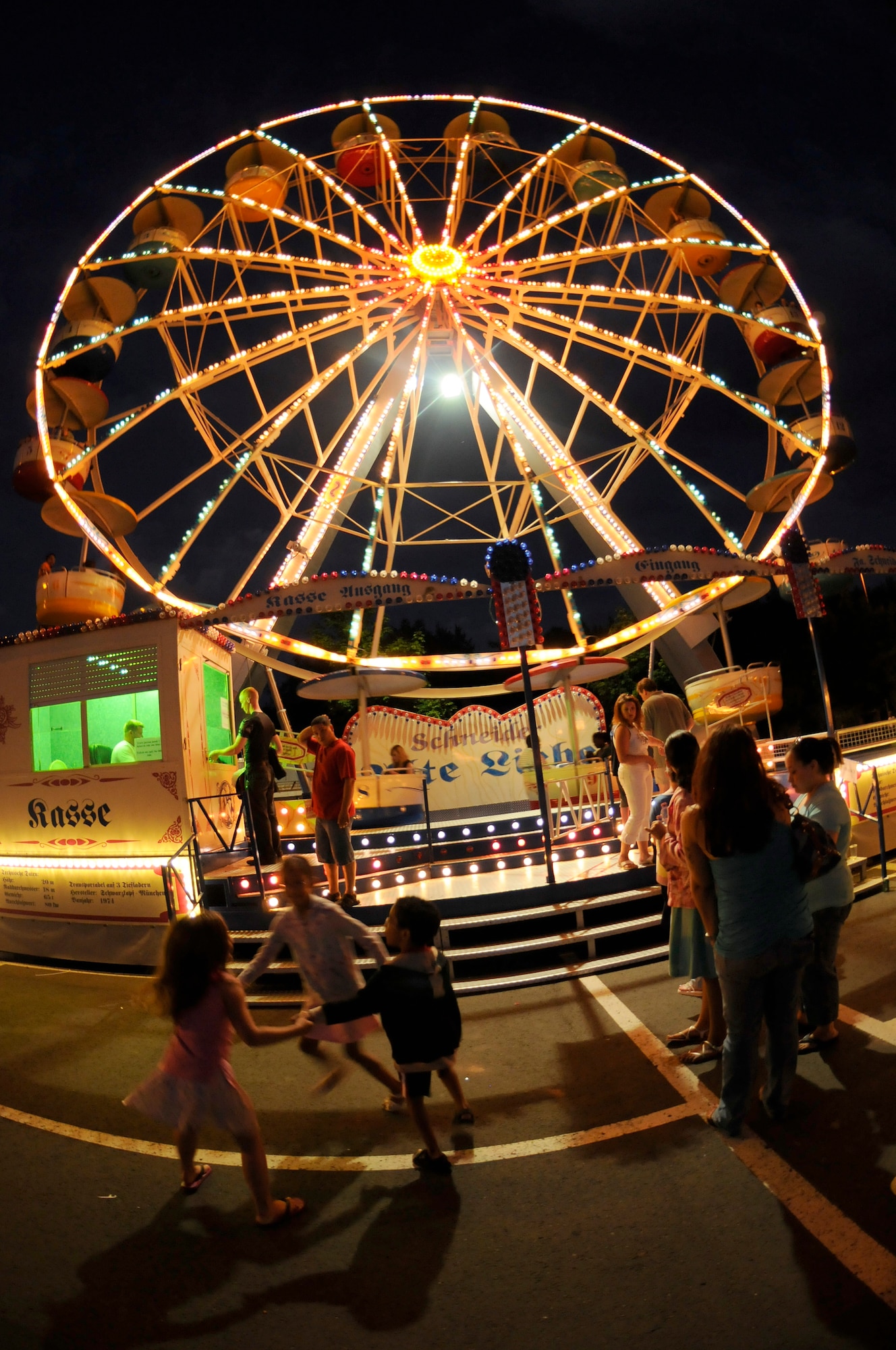 Children play a circle game before getting on the Ferris wheel, July 4, 2009, Kapaun Air Station, Germany. Kaiserslautern Military Community members celebrated the Rockin’ Fourth of July event with games, rides and concerts and ended the night with fireworks. (U.S. Air Force photo by Tech. Sgt. Kenneth Bellard)