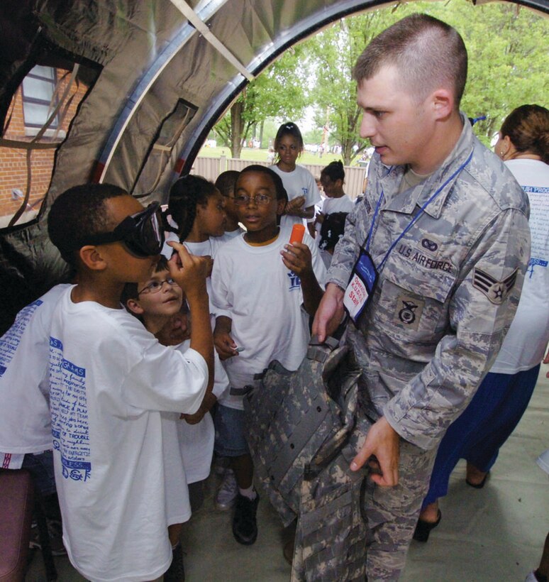 Senior Airman Patrick Harris, 316th Security Forces Squadron supply clerk, explains the function of night vision goggles to Antone Perry, 8, as Xavier Treadwell, 9, center, observes, while going through a mobility line. Antone is the son of Coast Guard Lt. Cmdr. Diane Perry, budget execution division financial manager, Coast Guard Headquarters, Washington D.C. Xavier is the son of Master Sgt. Patricia Treadwell, 779th Medical Support Squadron pharmacy flight superintendent. (U.S. Air Force photo/ Bobby Jones)