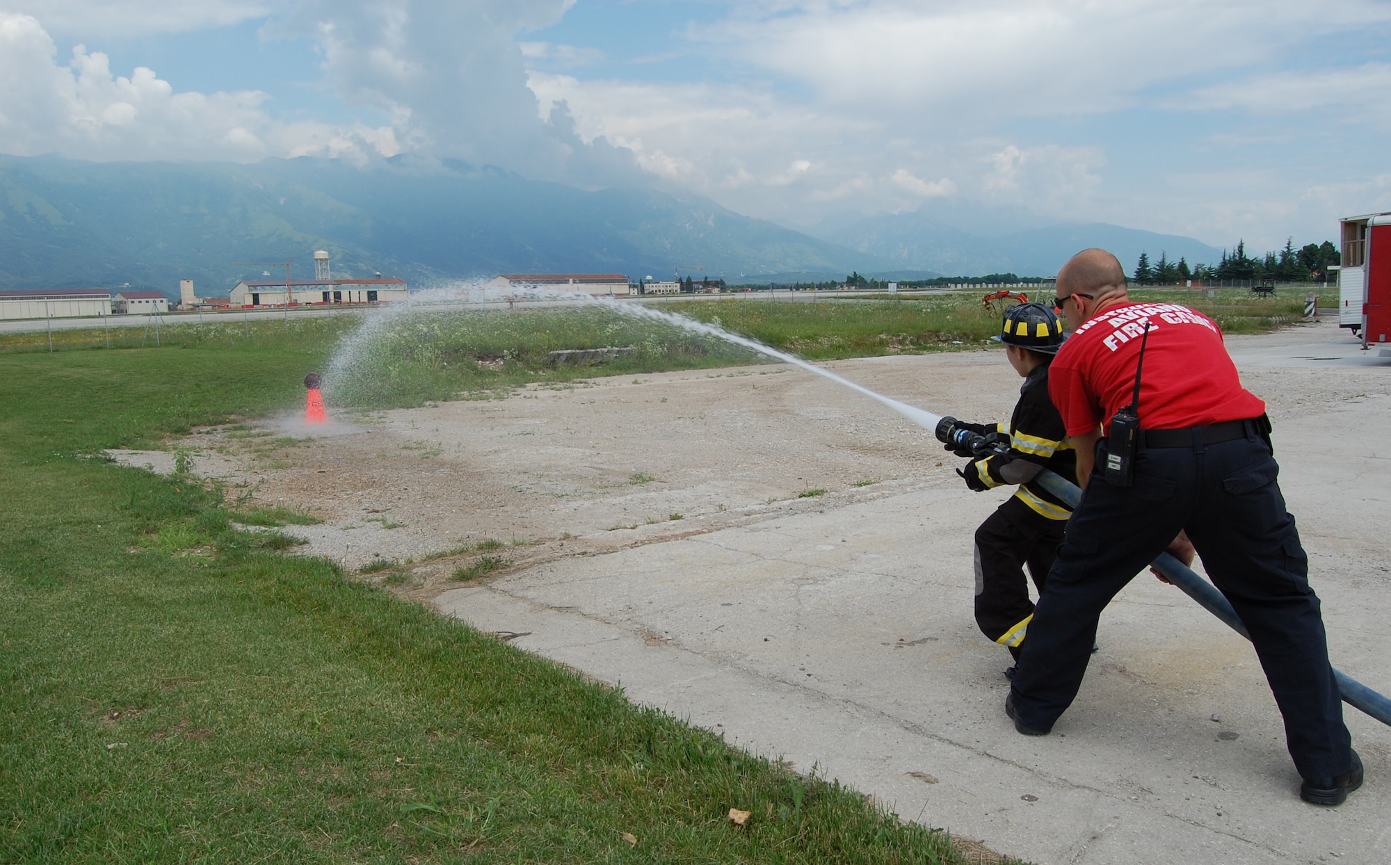 Staff Sgt. Joe Mauro, 31st Civil Engineer Squadron firefighter and Red Team leader, helps team member Cody Gummerson spray a basketball off of a cone as part of the Aviano Fire Camp relay competition July 3, 2009. The week-long camp, which was open to 10-13-year-old base children, taught attendees basic firefighter knowledge and skills. (U.S. Air Force photo/Staff Sgt. Lindsey Maurice)