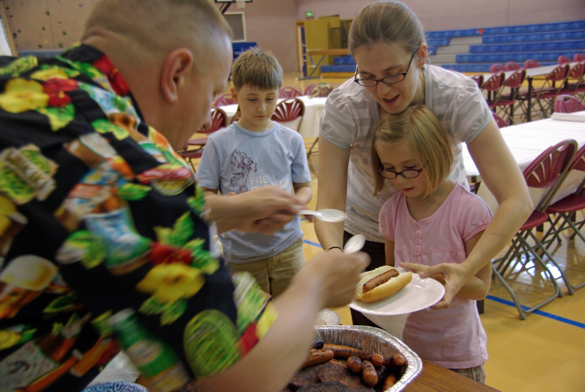 Senior Master Sgt. Brian Lyga, 352nd Special Operations Squadron, hands a hot dog to 7-year-old Abby McCurter as her mother Holly helps. Mrs. McCurter, wife of Tech. Sgt. Harley McCurter, 100th Civil Engineer Squadron, and her family were one of more than 15 families who attended the Hearts Apart dinner June 30 at the Mildenhall Youth Center here. Hearts Apart dinners are held monthly for family members of all Team Mildenhall's temporary duty, remote and deployed members. The next Hearts Apart dinner is July 30 at 5:30 p.m. in Heritage Park. For more information, call 01638543406. Sign ups taken through July 20. (U.S. Air Force photo by Tech. Sgt. Marelise Wood)