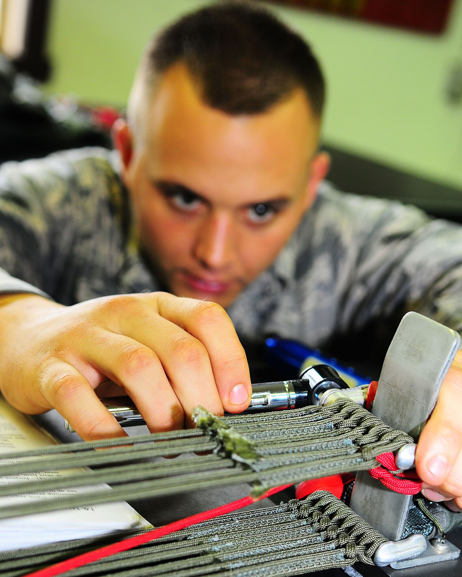 YOKOTA AIR BASE, Japan-- Airman Devin Ballesteros, 374th Operations Support Squadron survival equipment flight, uses a magnifying glass to check for hairline cracks in the connector link July 2. For safety purposes a parachute is repacked every 180 days. The survival equipment shop repacks approximately six parachutes a week. (U.S. Air Force photo/Airman 1st Class Michael Dillon)