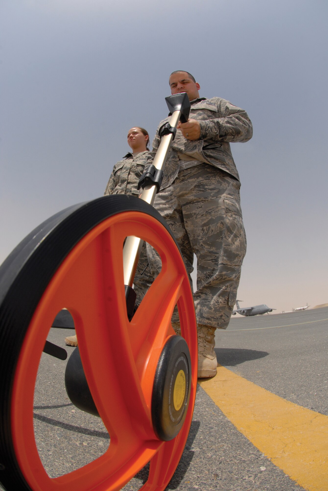 Staff Sgts. Myshel Rush, 379th Expeditionary Operations Support Squadron airfield management supervisor, and Nicholas Giaimo, 379th EOSS deputy airfield manager, use a measuring wheel to determine an area on the flightline for wing tip clearance June 30, here. Sergeant Rush hails from Lawton, Okla., and is deployed from Davis Monthan Air Force Base, Ariz.  Sergeant Giaimo hails from Lewisville, Texas, and is deployed from Elmendorf Air Force Base, Alaska. Both Airmen are deployed in support of Operations Iraqi, Enduring Freedom and Combined Joint Task Force - Horn of Africa.  (U.S. Air Force photo/Senior Airman Andrew Satran) 