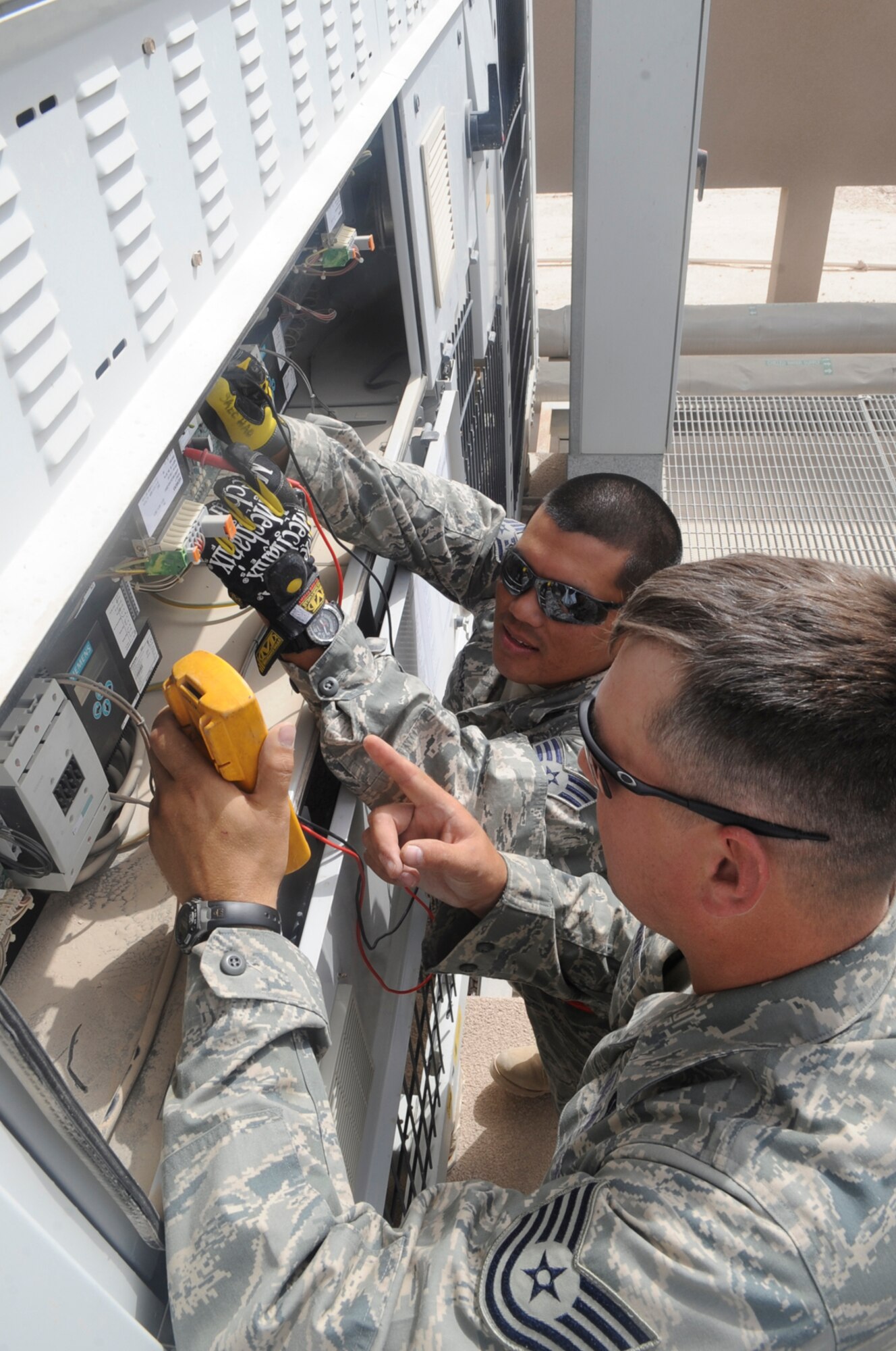 Senior Airman Kaota Saecho (rear) and Tech. Sergeant Joe Osborne, 379th Expeditionary Civil Engineer Squadron heating, ventilation, air-conditioning and refrigeration technicians, check the voltage July 2 on chiller that provides cool air to the Combined Air Operations Center at this air base in Southwest Asia. Airman Saechao is a native of Redding, Calif., and is deployed from Luke Air Force Base, Ariz., while Sergeant Osborne hails from Newton, N.J., and is stationed at Andrews Air Force Base, M.D.  (U.S. Air Force photo/Staff Sgt. Joshua Garcia)