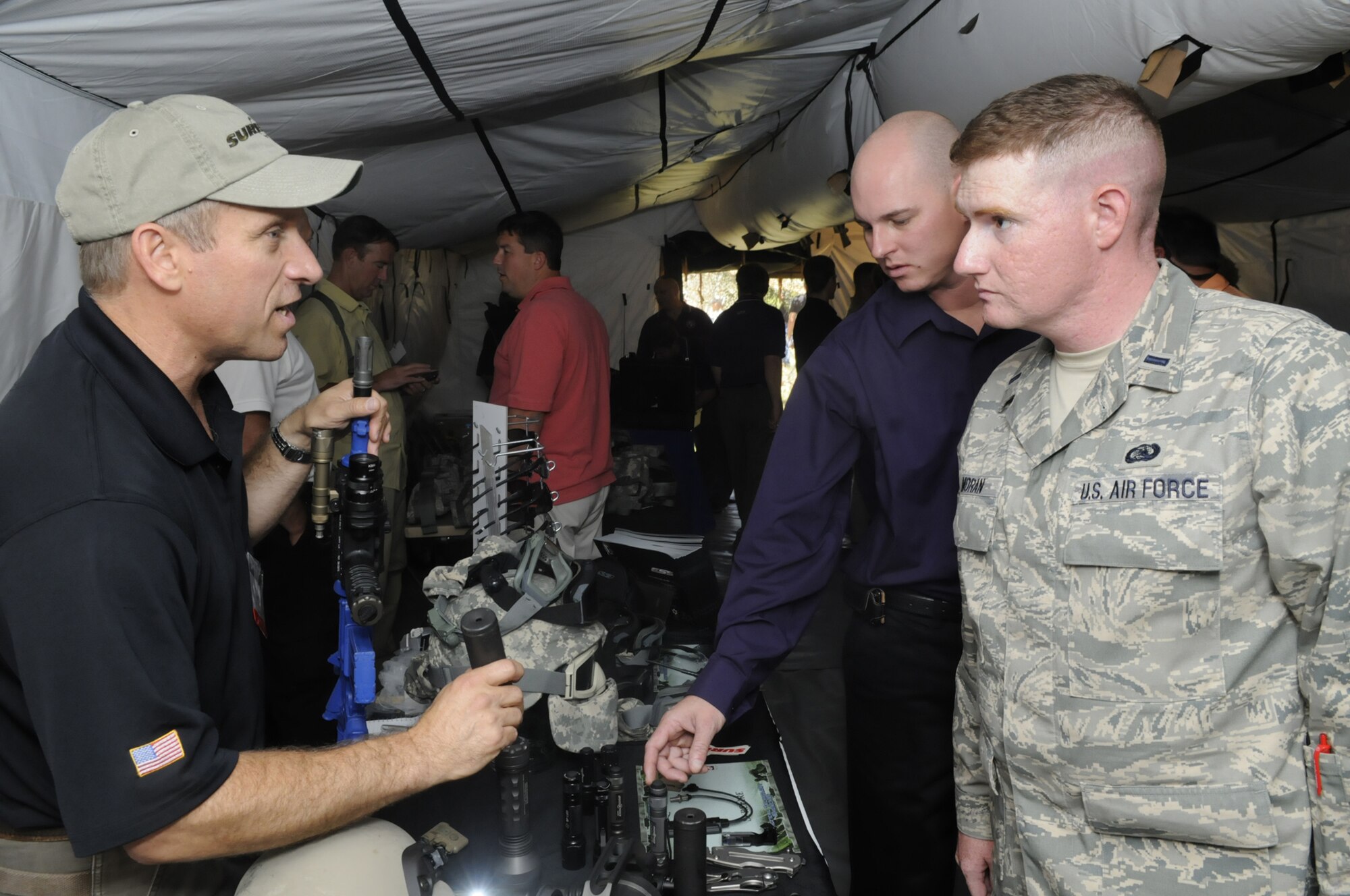 Rocky Senatore of Surefire demostrates some flashlights for Jason Sanders and 1st Lt. Andrew Moran at the Tactical Technology Showcase July 1. Visitors were exposed to  technologies such as weaponry, protective shelters, communications and surveillance and reconnaissance equipment. More than 60 exhibitors participated in the event hosted by the 5th Combat Communications group. U. S. Air Force photo by Sue Sapp