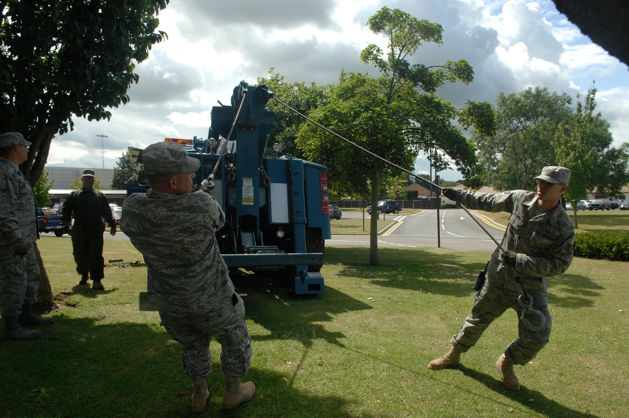 Staff Sgts. Kenneth Fewell (left) and Ryan Johnson, both of the 100th Logistics Readiness Squadron, pull steel winch cables from a 34-ton wrecker toward the accident scene of an overturned water tanker on RAF Mildenhall, England, July 8 near the roundabout on Hawaii Street. The Mildenhall Fire Department's 4,000-gallon water tanker overturned while responding to a call. (U.S. Air Force photo by Senior Airman Thomas Trower)
