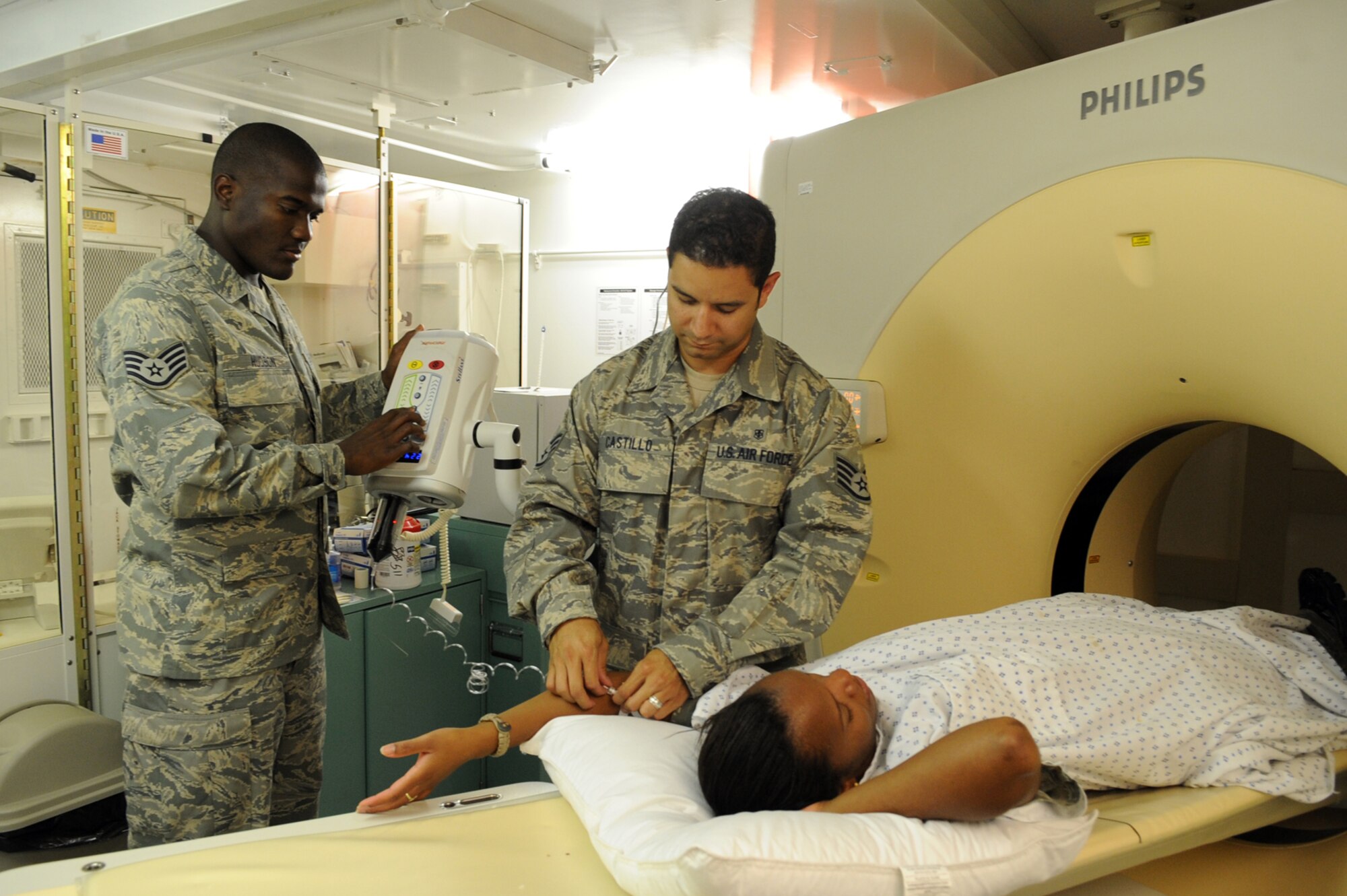 Center, Staff Sgt. Brian Castillo, 379th Expeditionary Medical Group radiology technologist, prepares a simulated patient for a scan with a computed tomography machine, as Staff Sgt. Trevor Hudson, 379 EMDG, checks the amount of contrast dye that will be injected during training. The scan will allow the technicians to see the patient’s internal organs. Sergeant Hudson is from Miami and deployed from th U.S. Air Force Academy, Colo. while Sergeant Castillo is from El Paso, Texas and is deployed from Travis Air Force Base, Calif.; both support Operations Iraqi Freedom, Enduring Freedom, and Combined Joint Task Force-Horn of Africa.(US Air Force photo/Staff Sgt. Joshua Garcia)