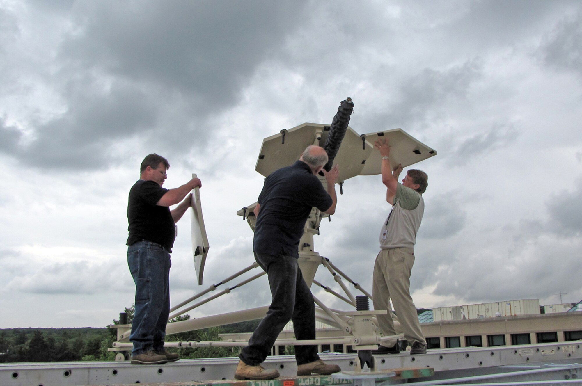 Members of a combined Electronic Systems Center-MITRE team assemble a Ground Multi-band Terminal antenna on the roof of a MITRE building in Bedford, Mass. Having a system available in the program office allows program experts to troubleshoot reported problems and review terminal changes and enhancements before they are sent to the field. (U.S. Air Force photo/Beth Farrington) 
