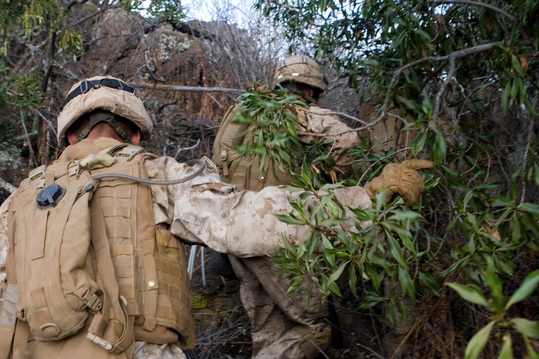 Dense brush, jagged lava rocks and steep hillsides challenged Marines as they tried to quickly and quietly move over a ridge to sneak up on an enemy compound.
