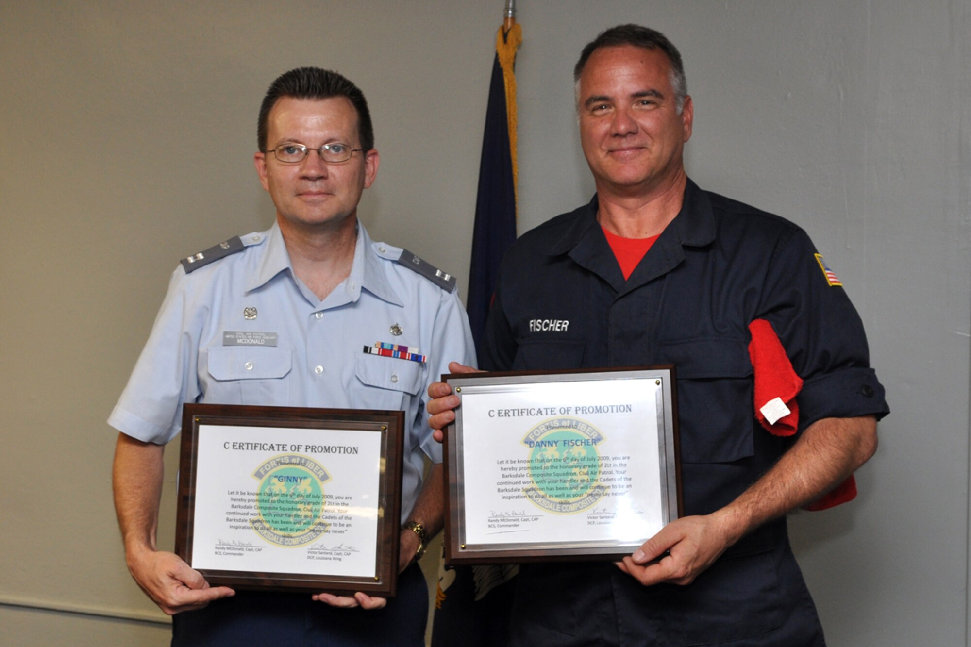 Capt. Randy McDonald, commander, Barksdale Composite Squadron, Civil Air Patrol, and Master Sgt. Danny Fischer, 917th Maintenance Squadron, armament shop, display honorary promotion certificates after Sergeant Fischer’s K-9 partner “Ginny” was promoted to the C.A.P. rank of 2nd Lt. in a ceremony at the Barksdale Air Force Base, La., C.A.P. Headquarters July 6, 2009. Sergeant Fischer and Ginny are volunteers with the Shreveport Fire Department K-9 Search and Rescue Task Force. Capt. McDonald was honored to stand- in for the photo since Ginny has no thumbs to hold the certificate. (U.S. Air Force photo/Tech. Sgt. Jeff Walston)