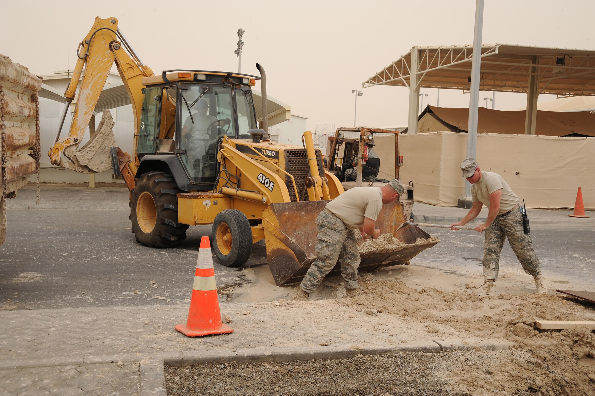 SOUTHWEST ASIA - Tech. Sgt. Shawn Ballor and Tech. Sgt. Klinton Bruck, 380th Expeditionary Civil Engineer Squadron, utility craftsmen, shovel excess dirt from a hole dug to find a leaking pipe into the front loader of a tractor, July 6 in Southwest Asia. The Airmen of the 380th ECES utilities flight replaced the mechanical joint on the flange to fix a leaking pipe. (U.S. Air Force photo by Senior Airman Brian J. Ellis)